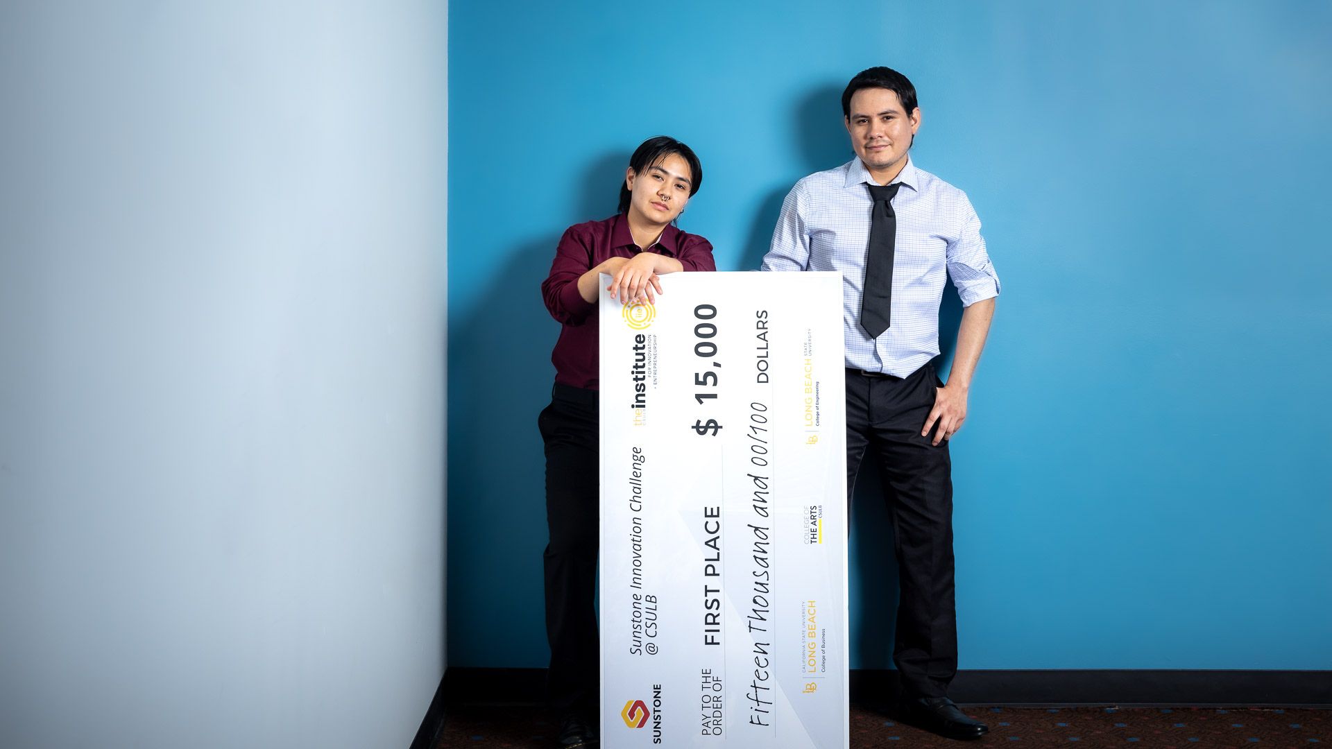 Winners of Sunstone Innovation Challenge Two people pose with an oversized $15,000 first place check against a blue wall.
