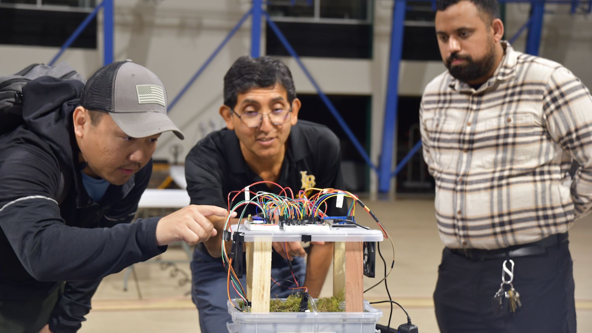 Three people examine a project with colorful wiring on a clear plastic base. Three people examine a project with colorful wiring on a clear plastic base.