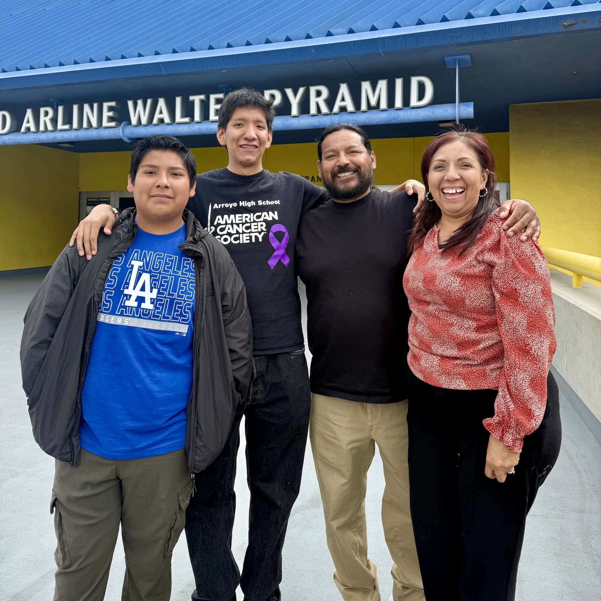 Four people smile in front of the blue Walter Pyramid at CSULB.