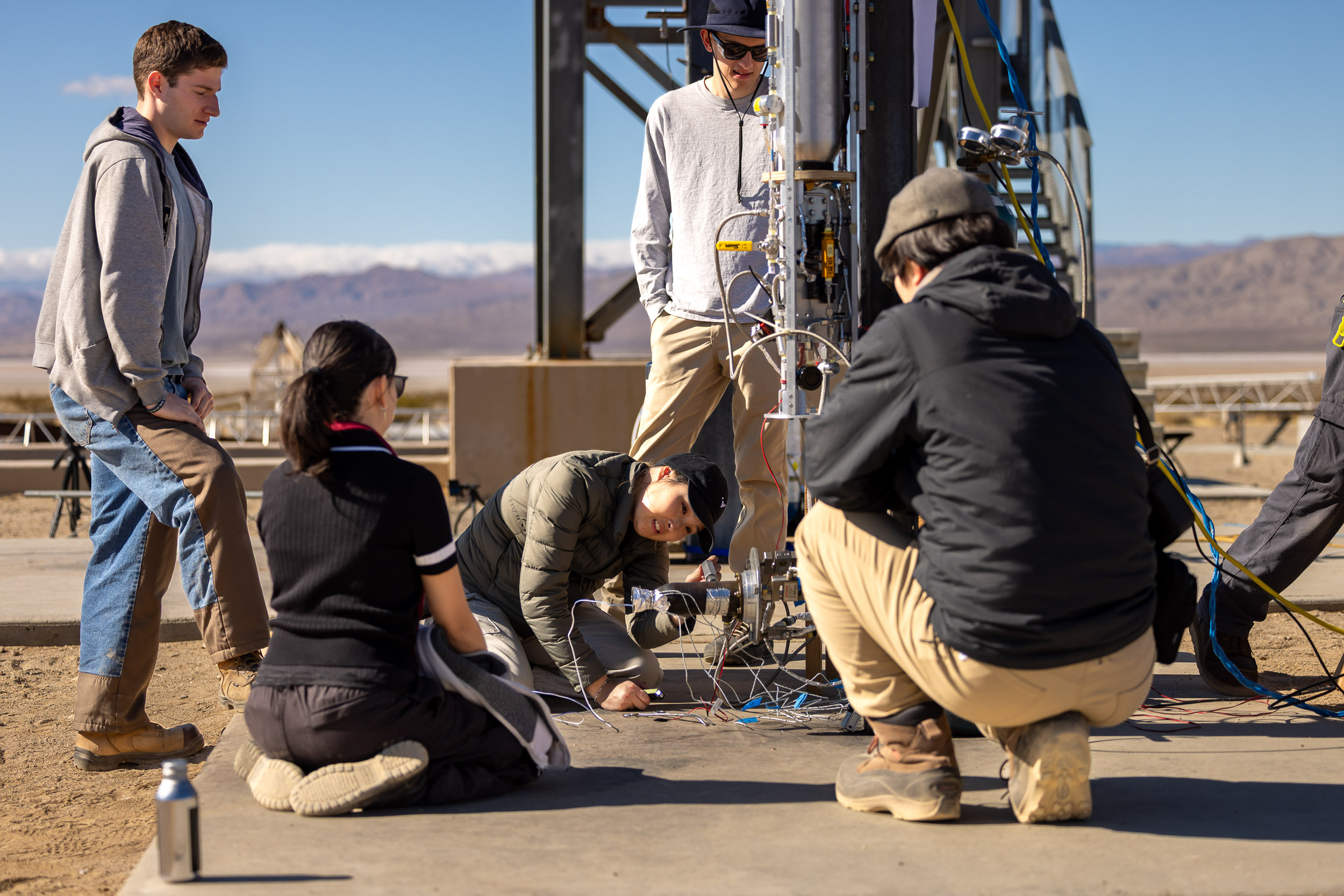 Students crouch down by the side of a rocket in the dessert