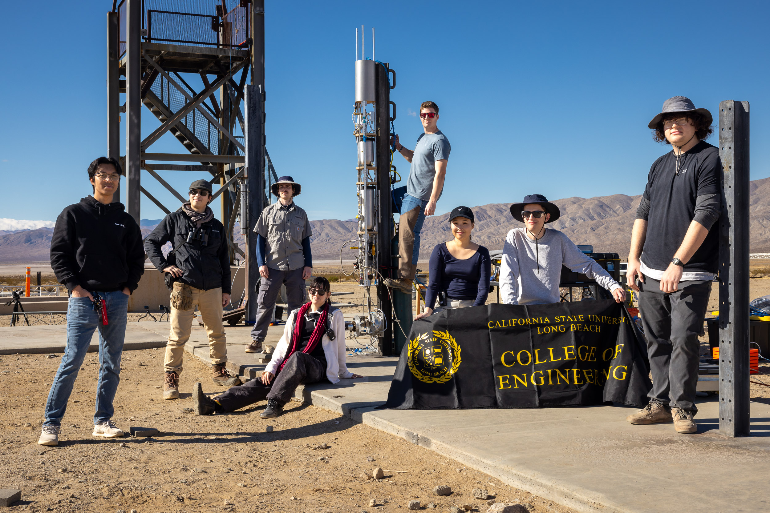 Eight people pose with a test stand and a banner reading "California State University Long Beach College of Engineering" in a desert setting