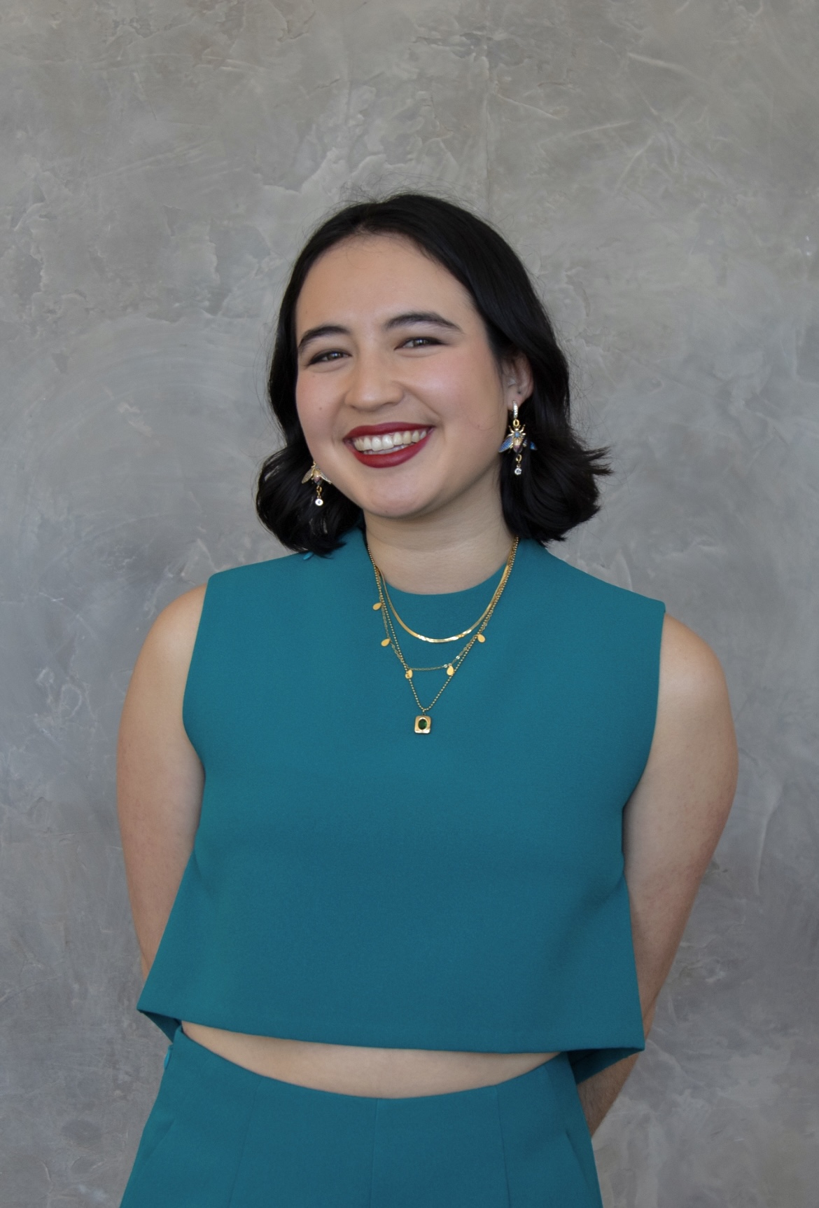 Light skinned female-presenting with short black hair and a teal outfit.