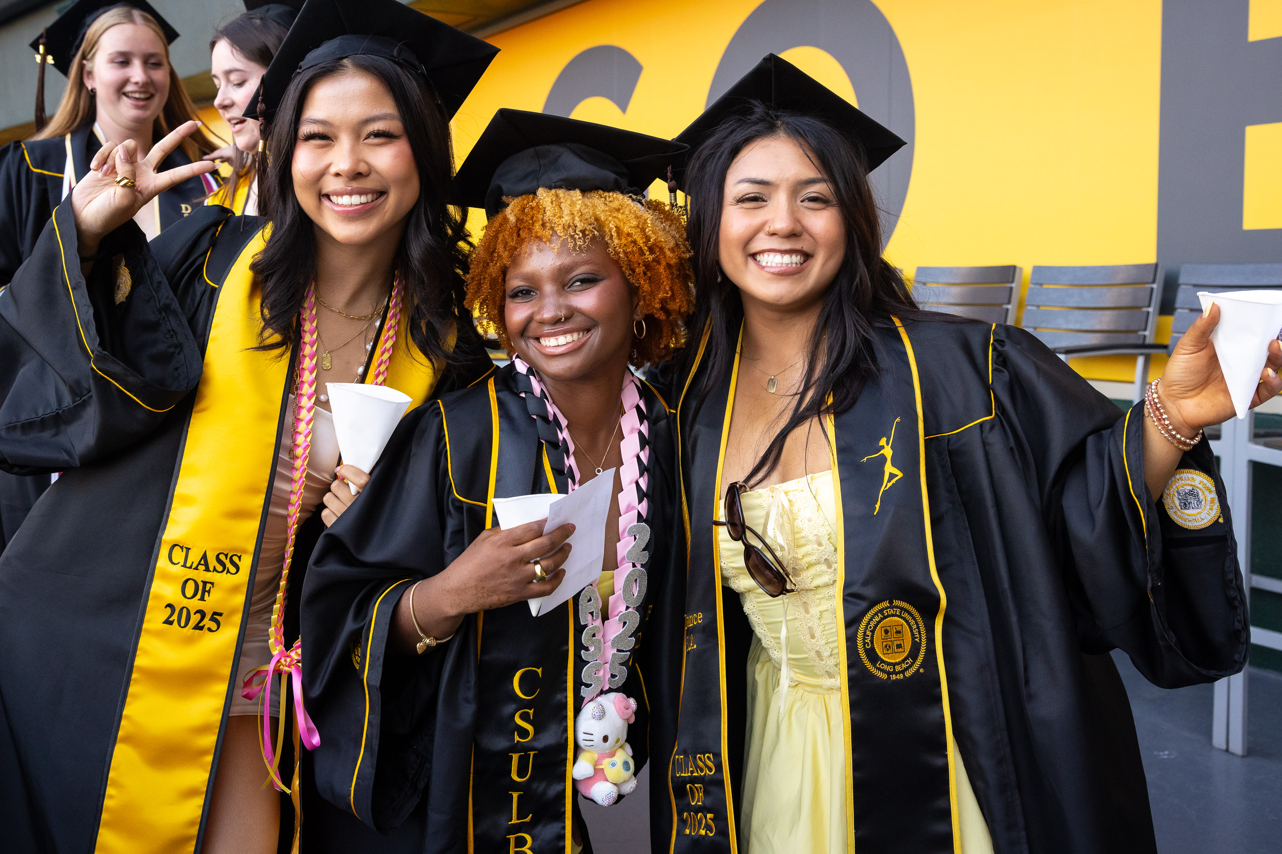 Three graduates smiling together at commencement.