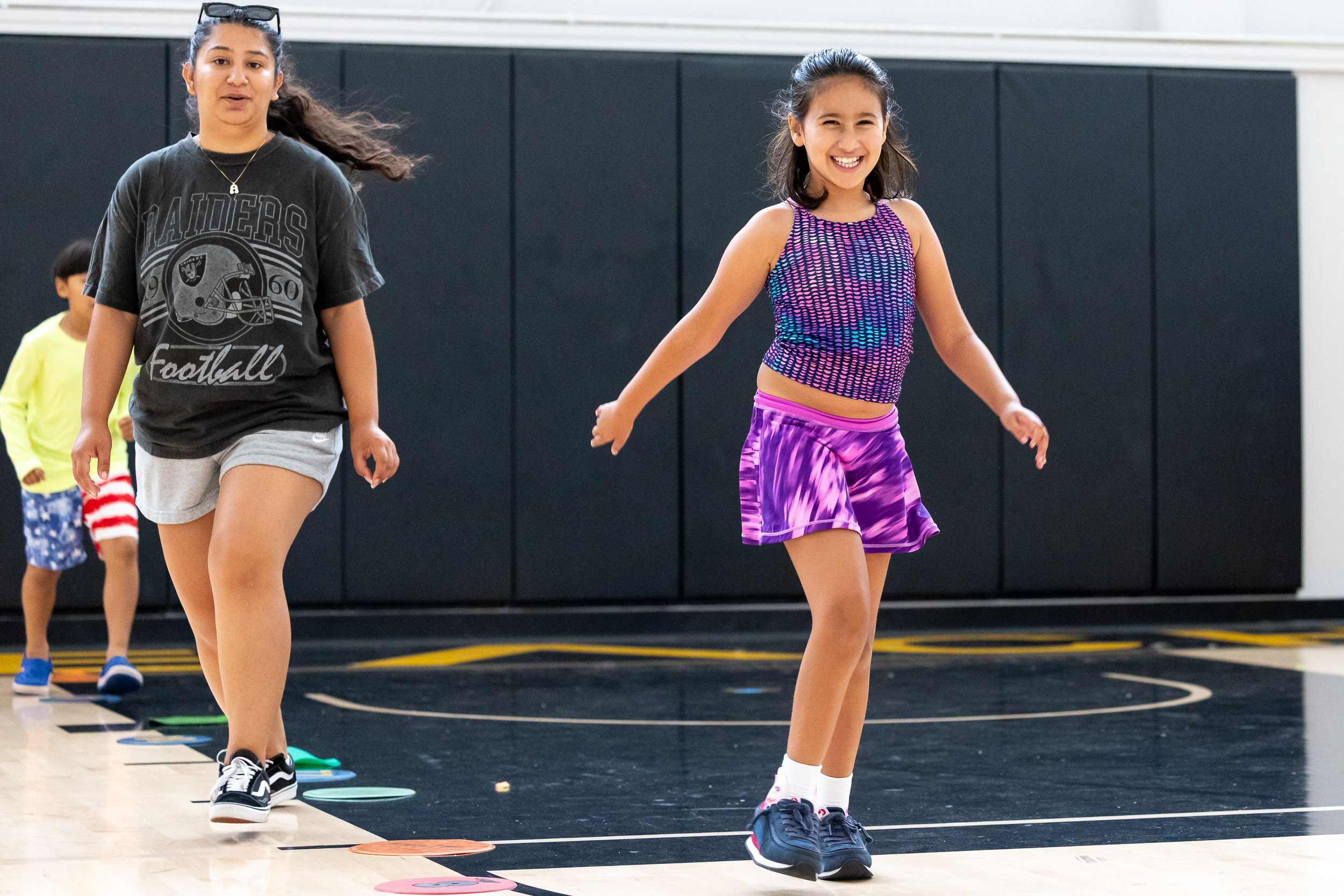A child smiles as she skips in a gym