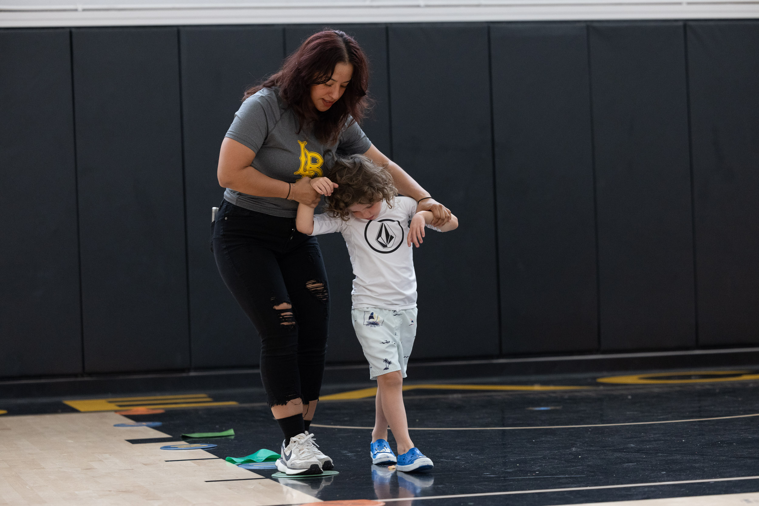 Adult helps child walk on gym floor during activity