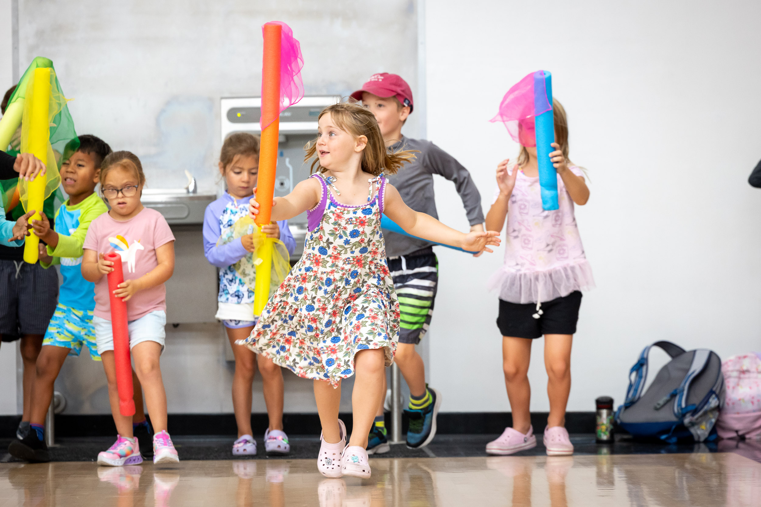 Group of children plays indoors with foam sticks and scarves