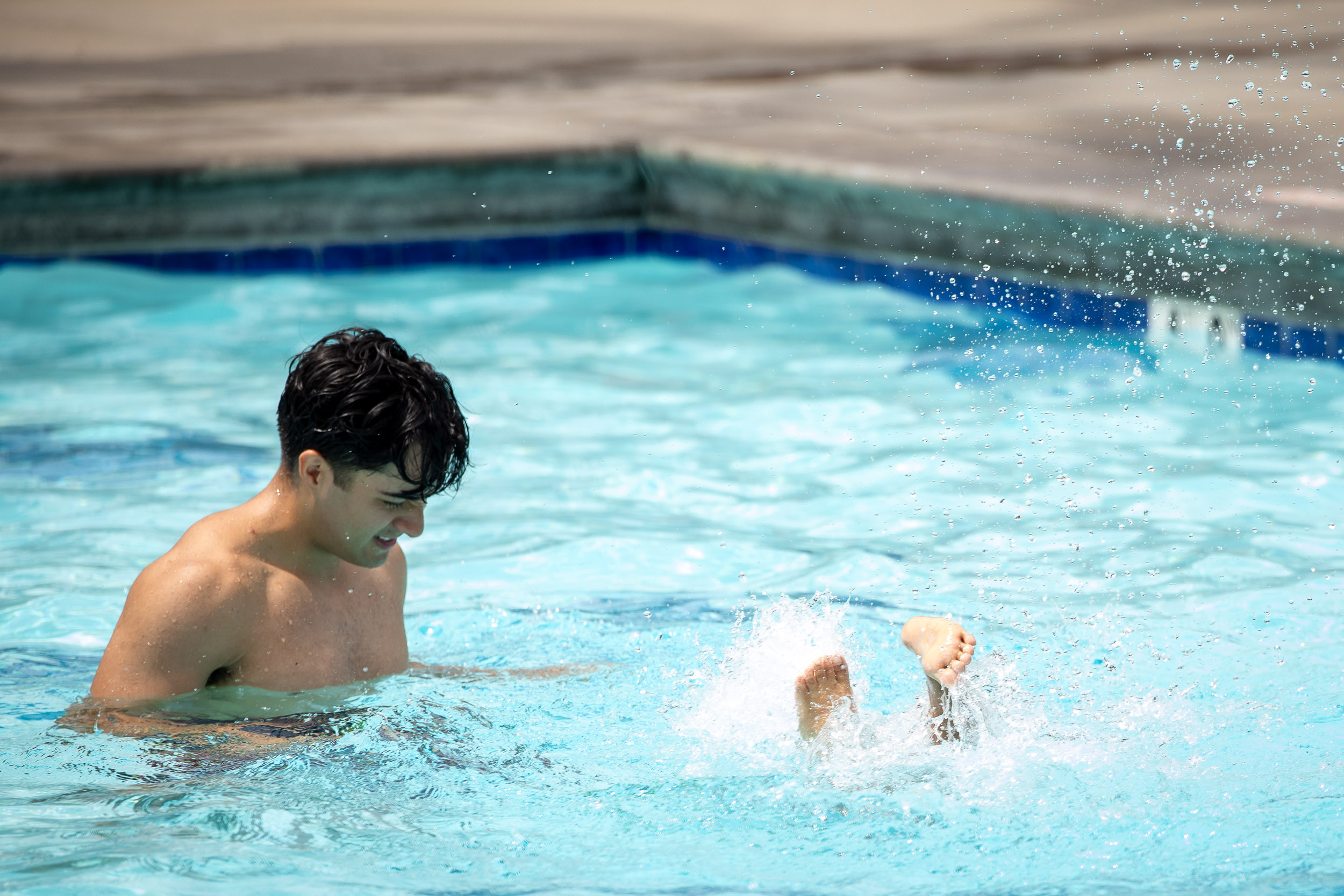 Young adult watches a child splashing feet in a pool
