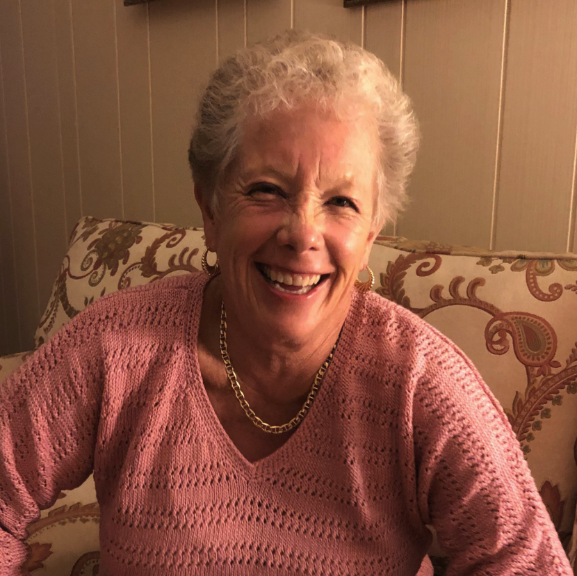 A person in a sweater smiles while seated on a sofa
