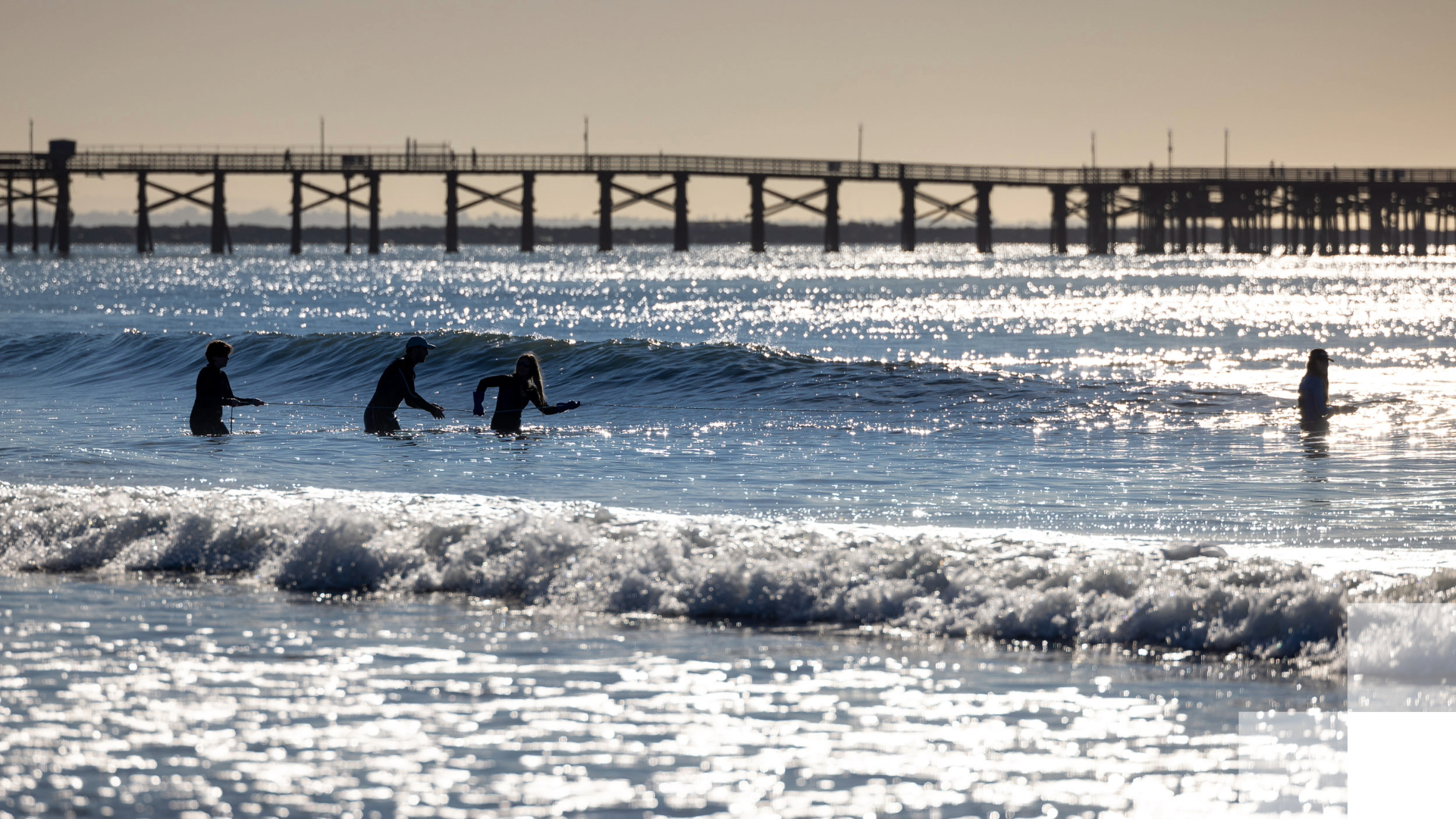 People wading in the ocean near a pier People wading in the ocean near a pier