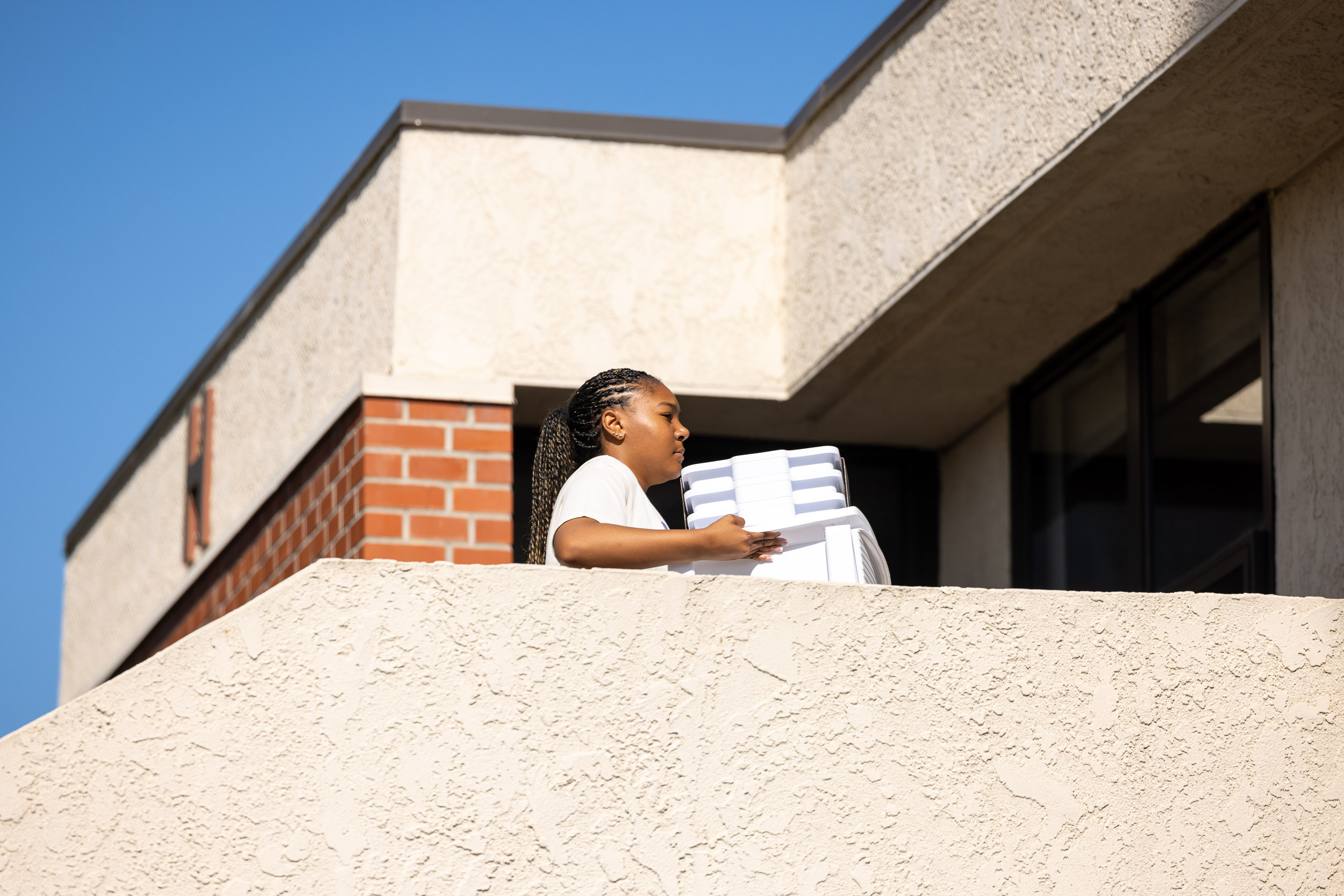 A person carries a large storage bin across grass near a brick building.