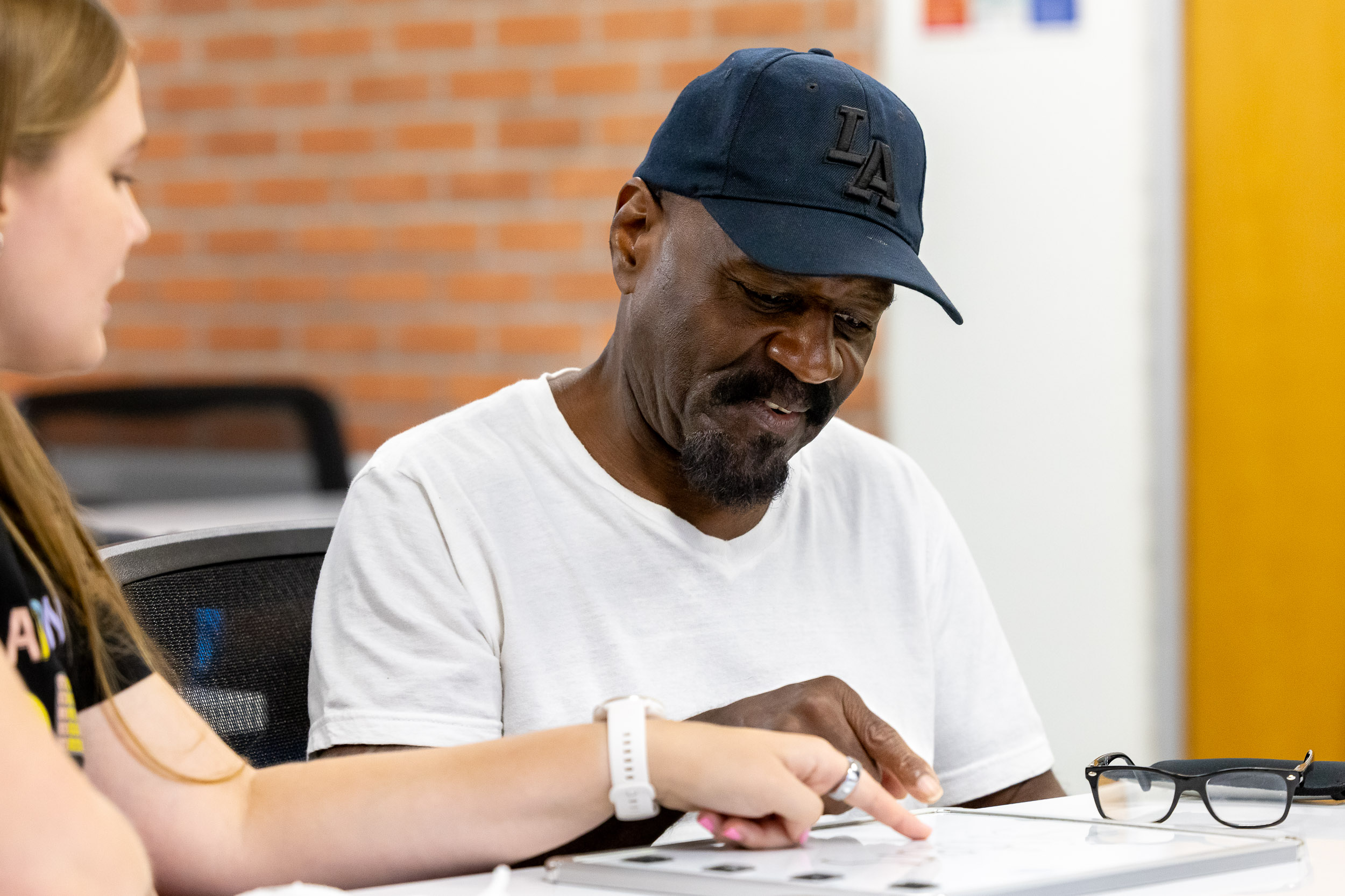 Two people sit at a table and point to a tablet during a class