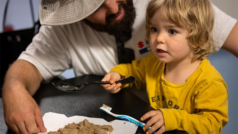 young child excavating through hard sand while teacher helps