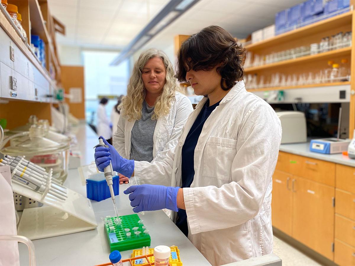 Jaylin in the lab using pipette as Dr. Fisher supervises