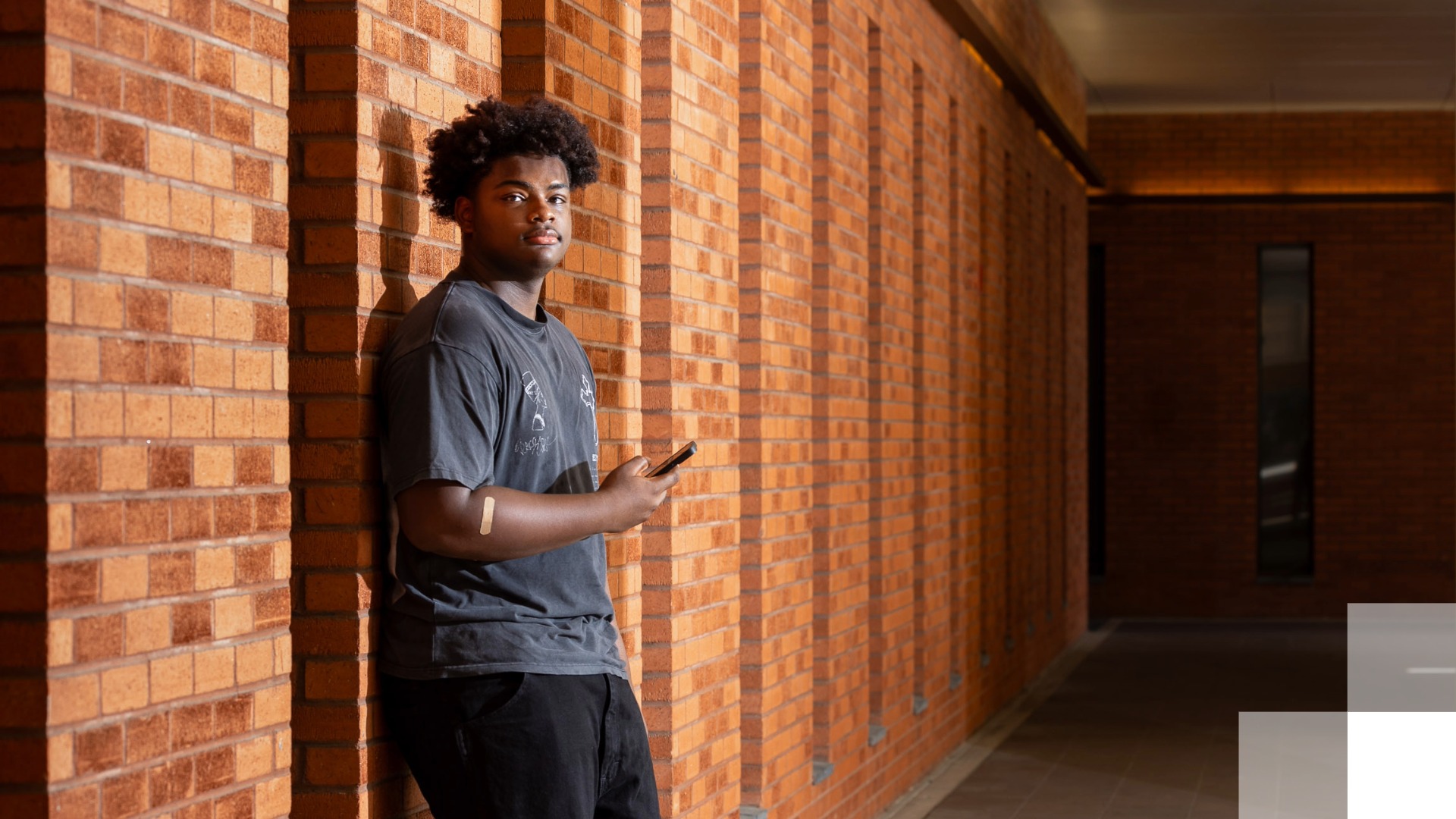 Student Communications Improvement Project Student leaning against a brick wall while holding a phone