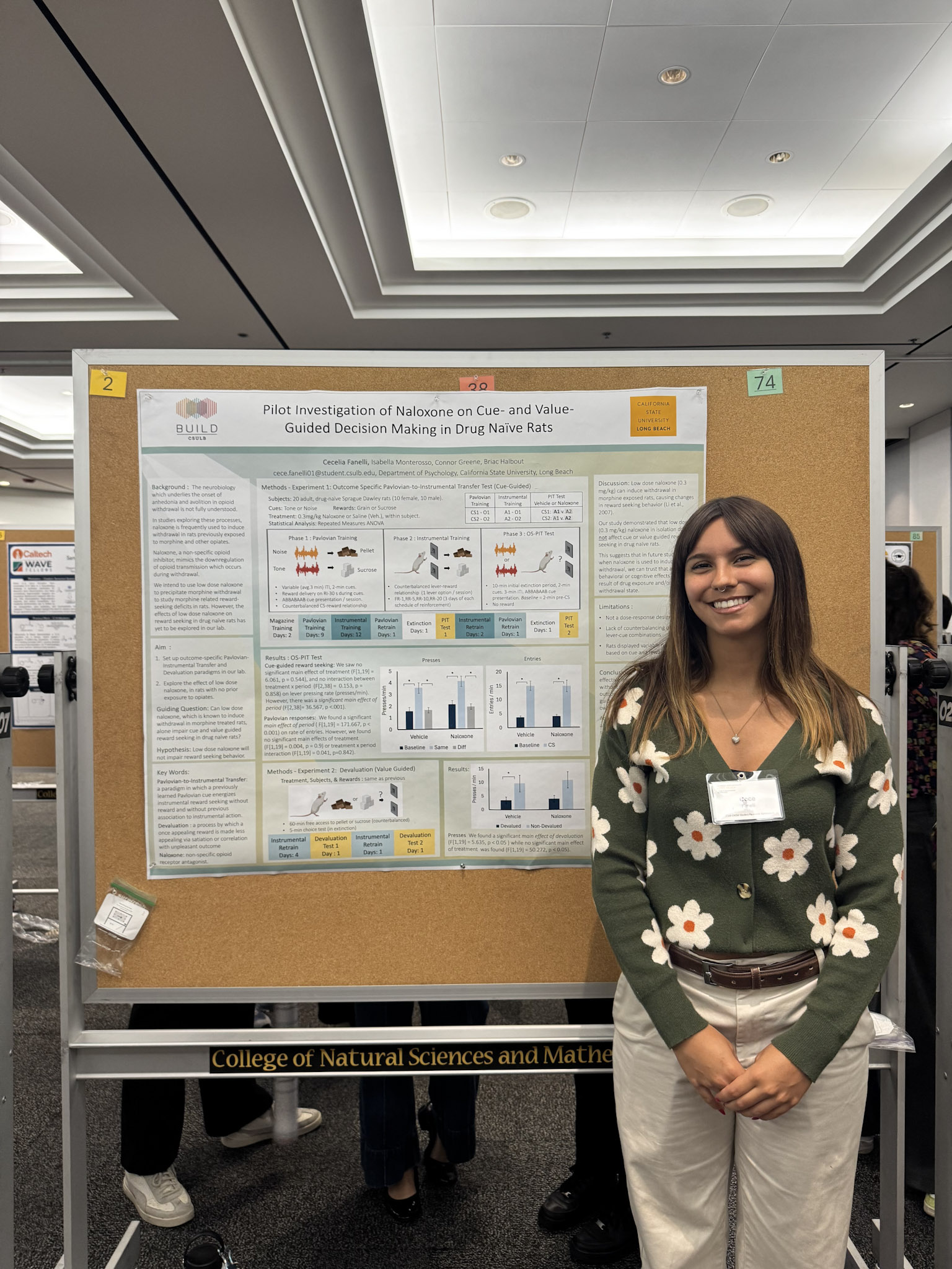 Female presenter with brown hair and green shirt with flowers standing in front of research poster