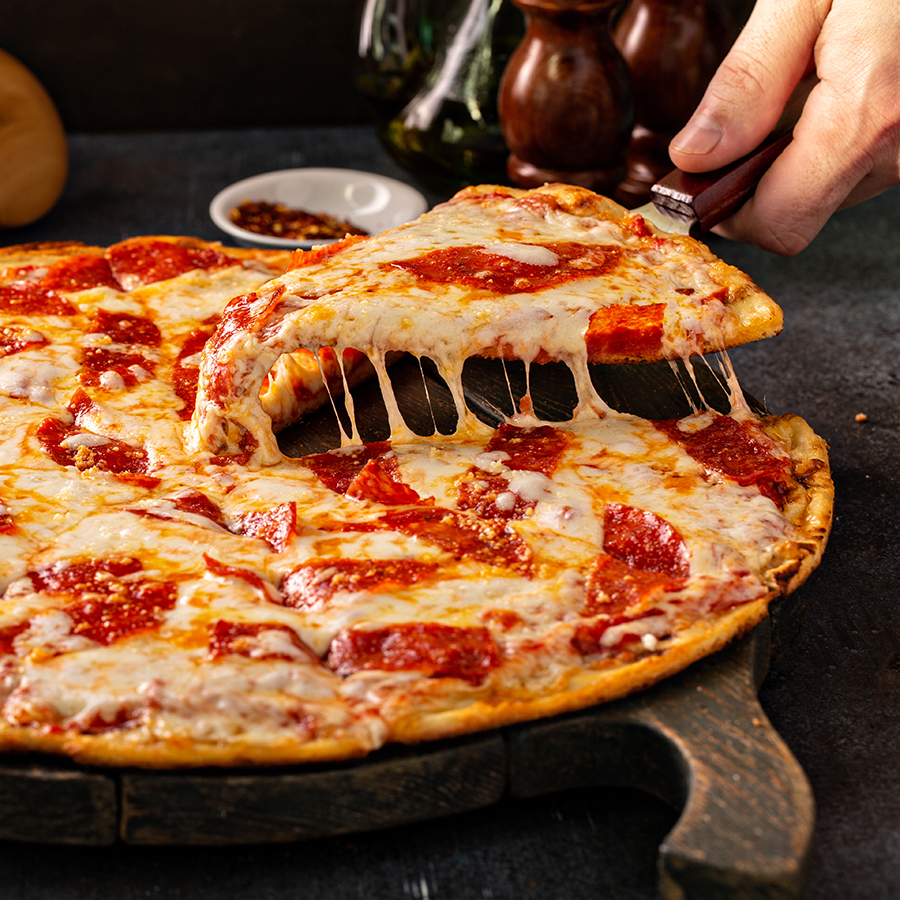 Slice of pizza being picked up and seperated from rest of pizza and showing a nice cheese pull. 