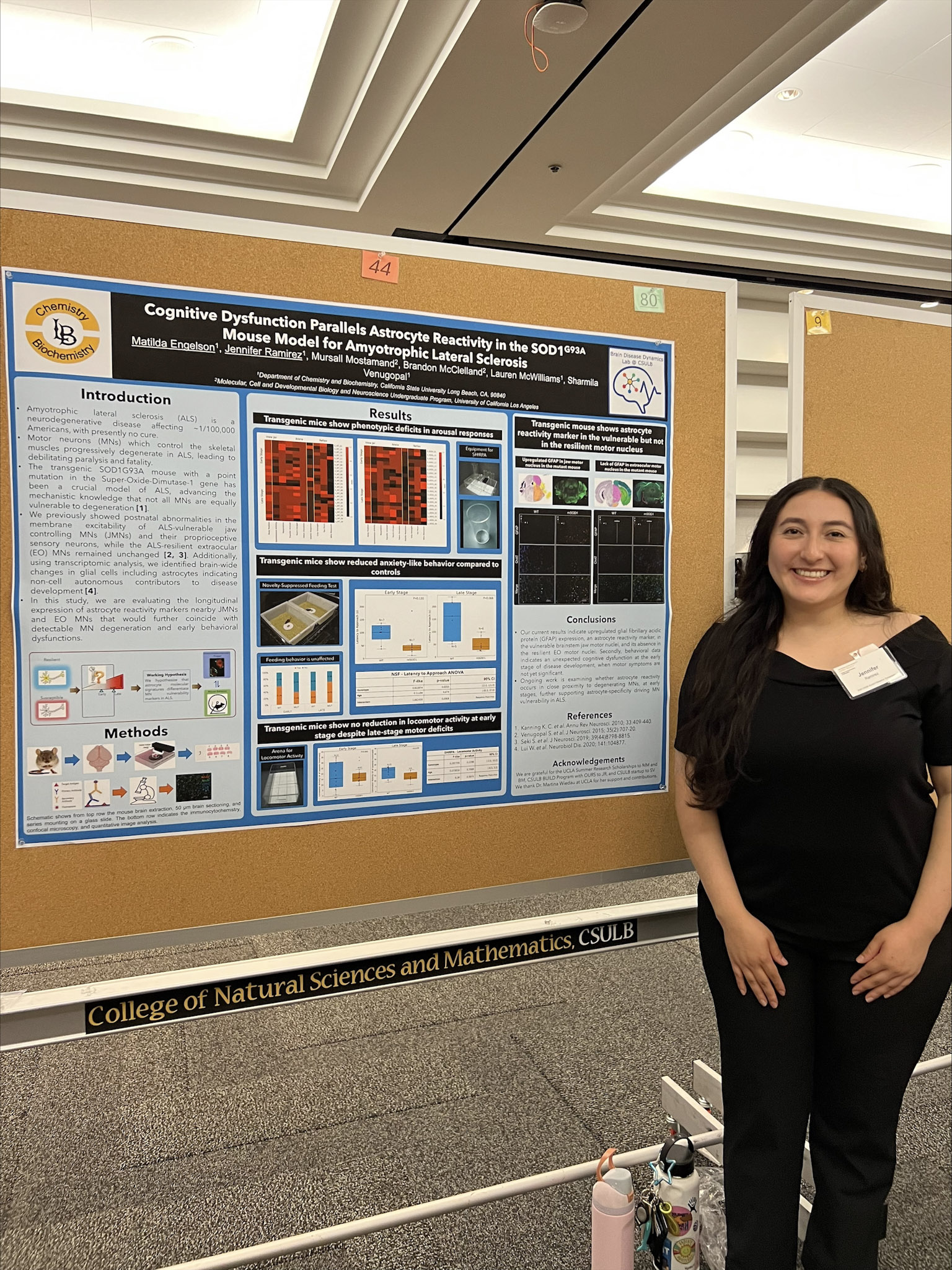 Female presenter with long black hair and black shirt standing in front of research poster