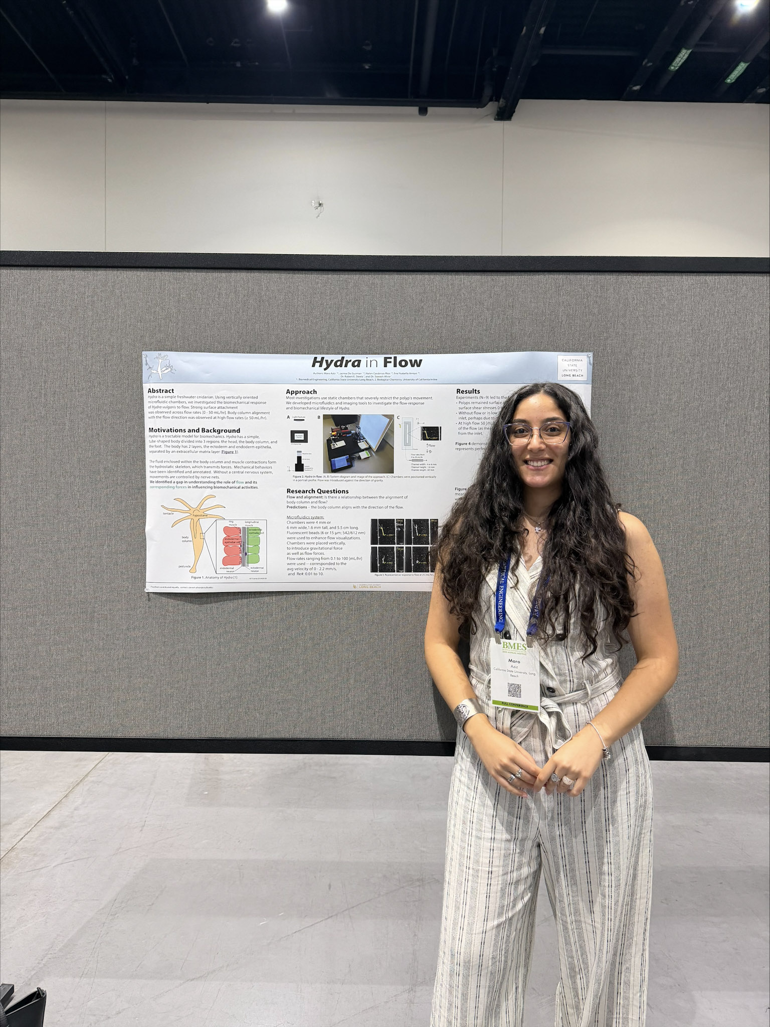 Woman with dark long hair and light outfit smiling and standing in front of scientific poster