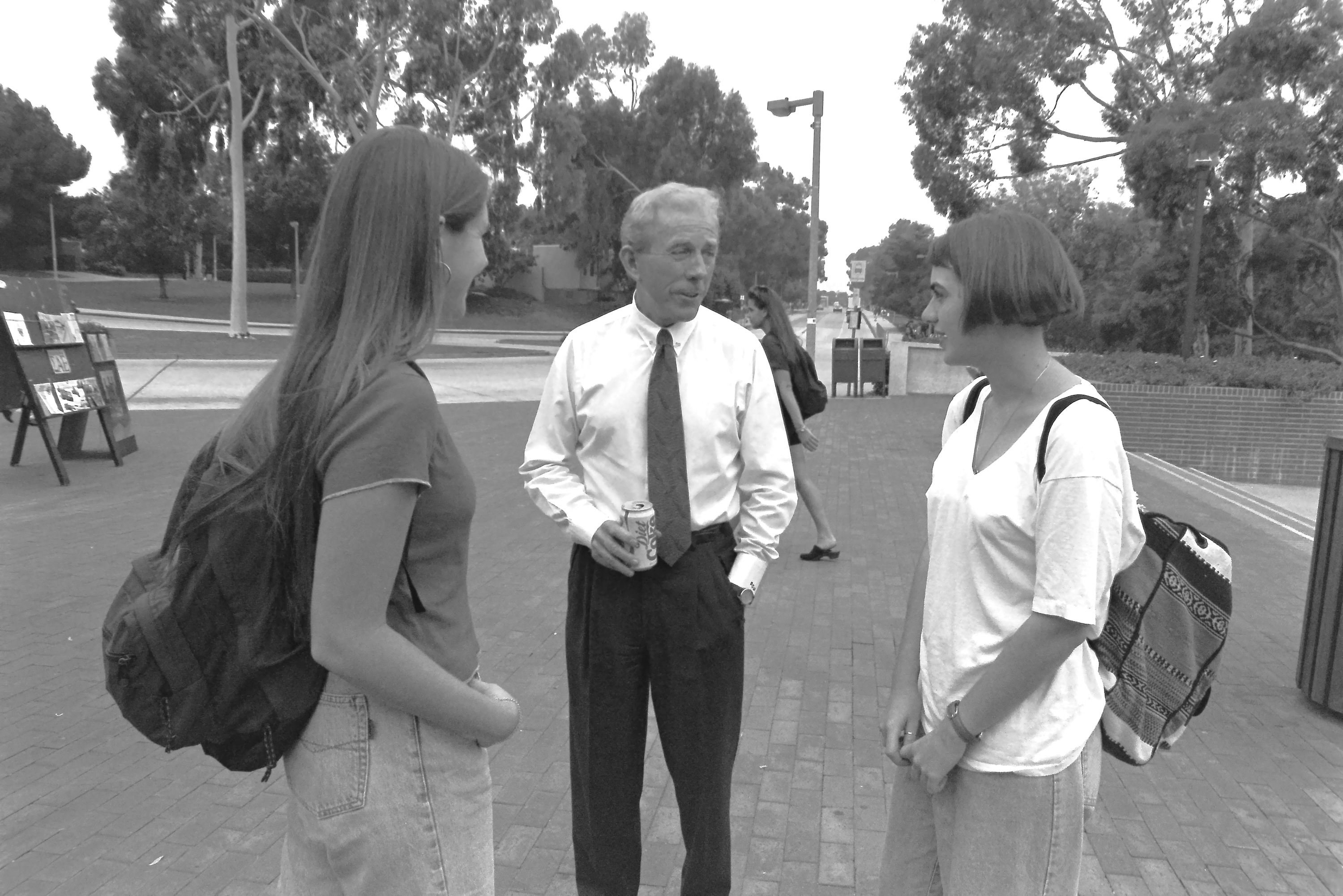 Man stands on campus speaking with two students