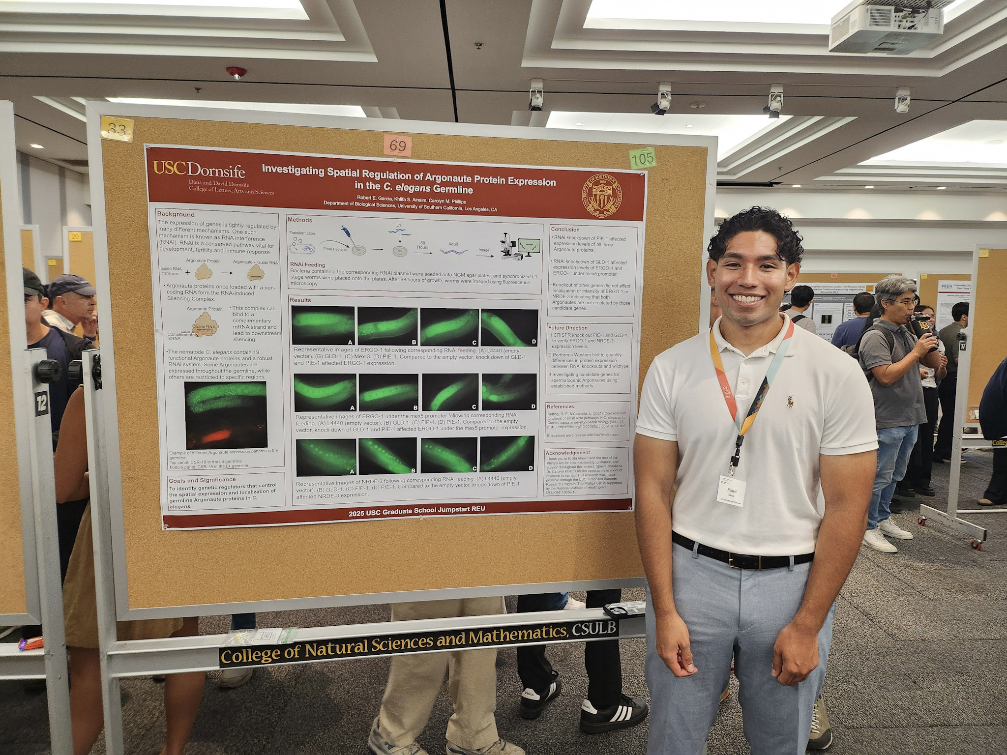 Male with black hair and light t-shirt standing in front of scientific poster