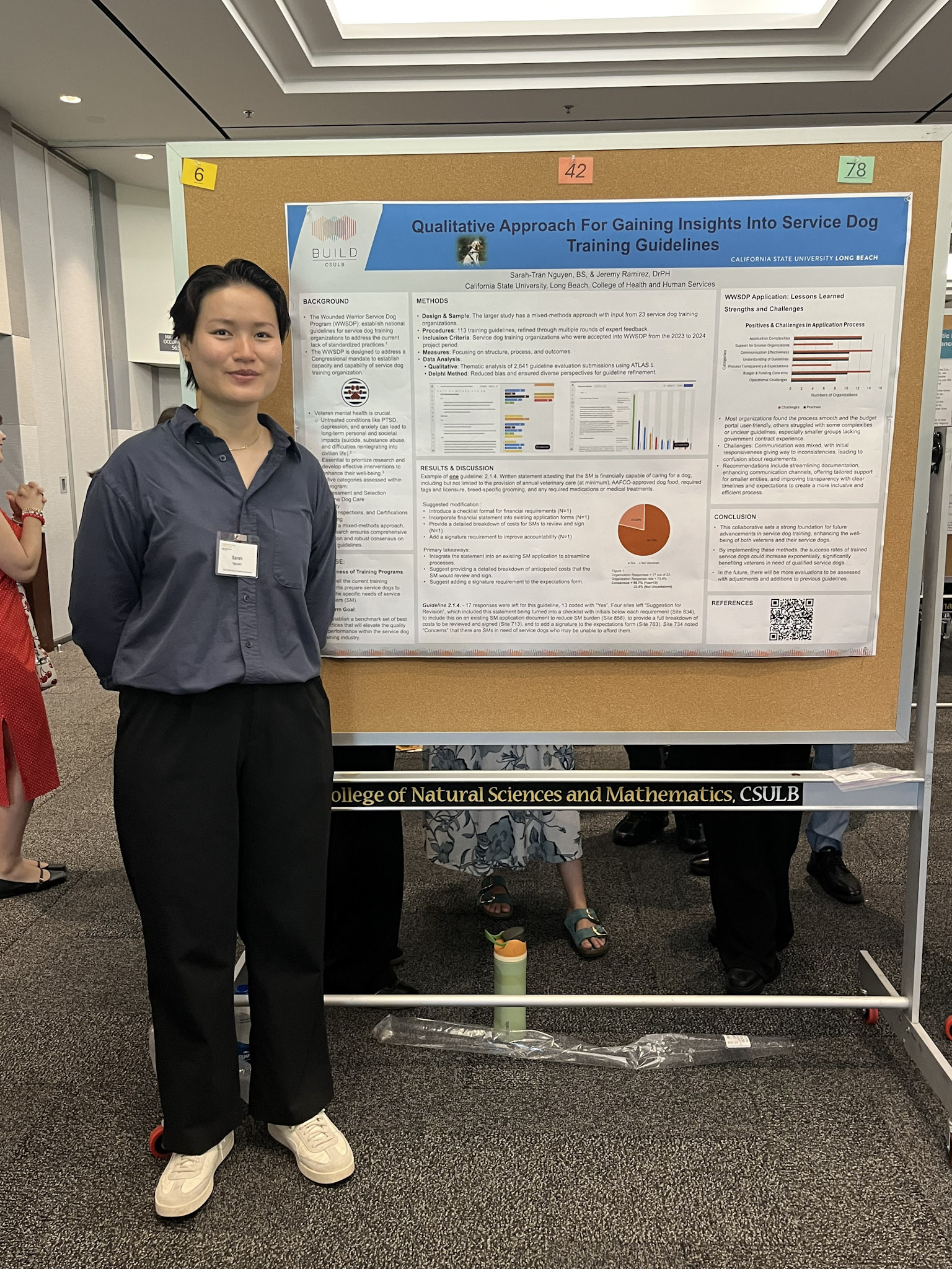 Female presenter with short black hair and blue shirt standing in front of research poster