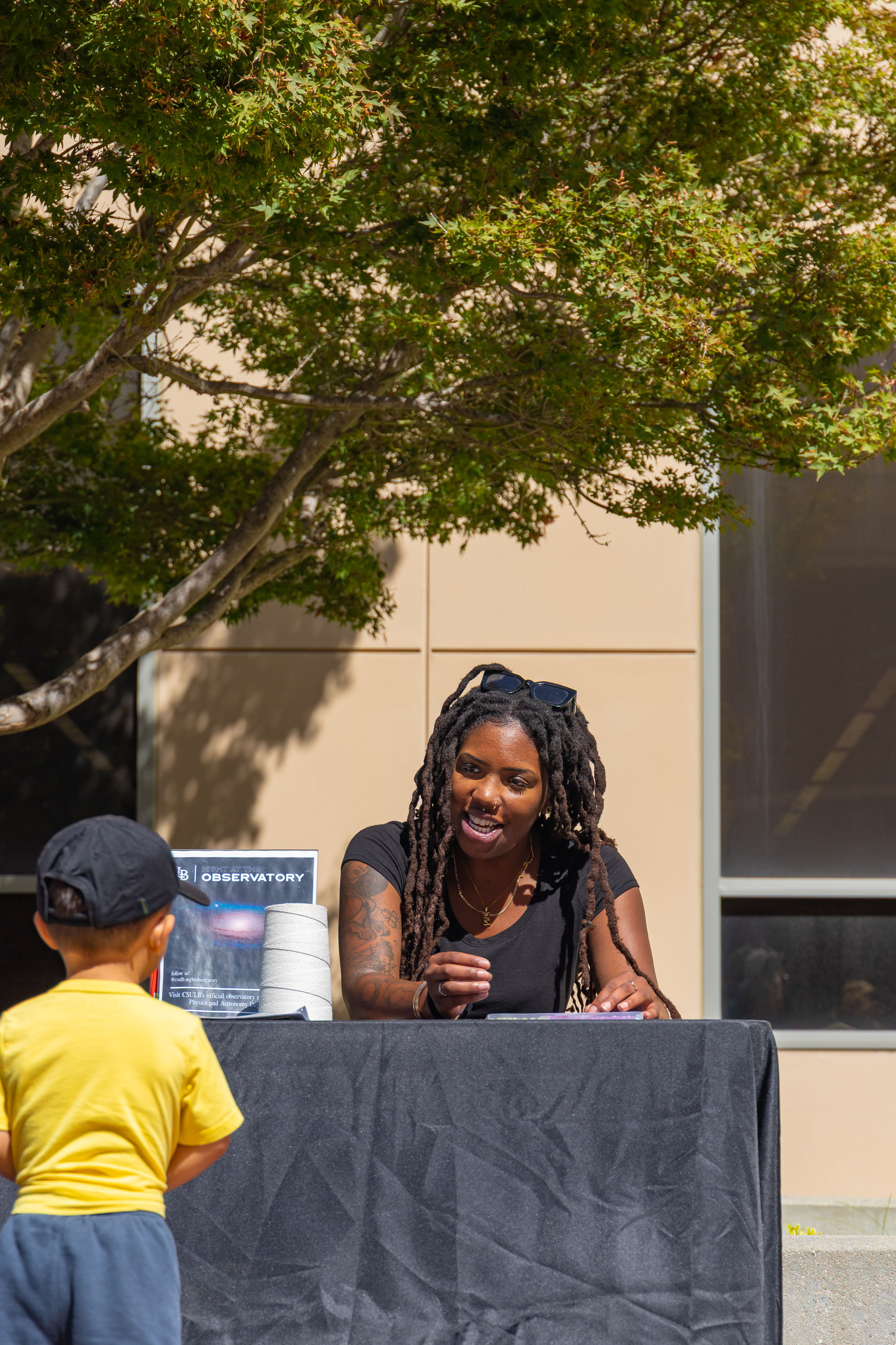 Student volunteer speaks with a child at an observatory table outside.