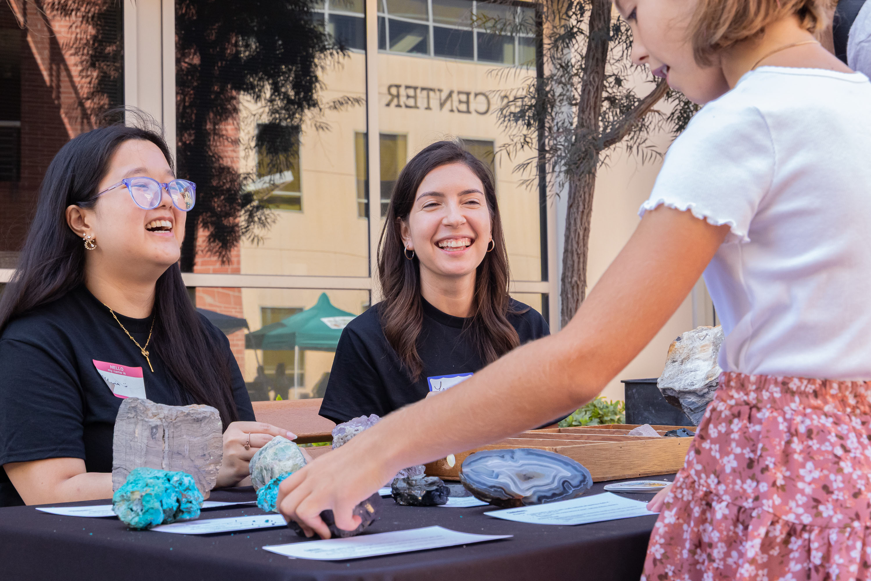 Two students share rock and mineral samples with a child at an outreach table.