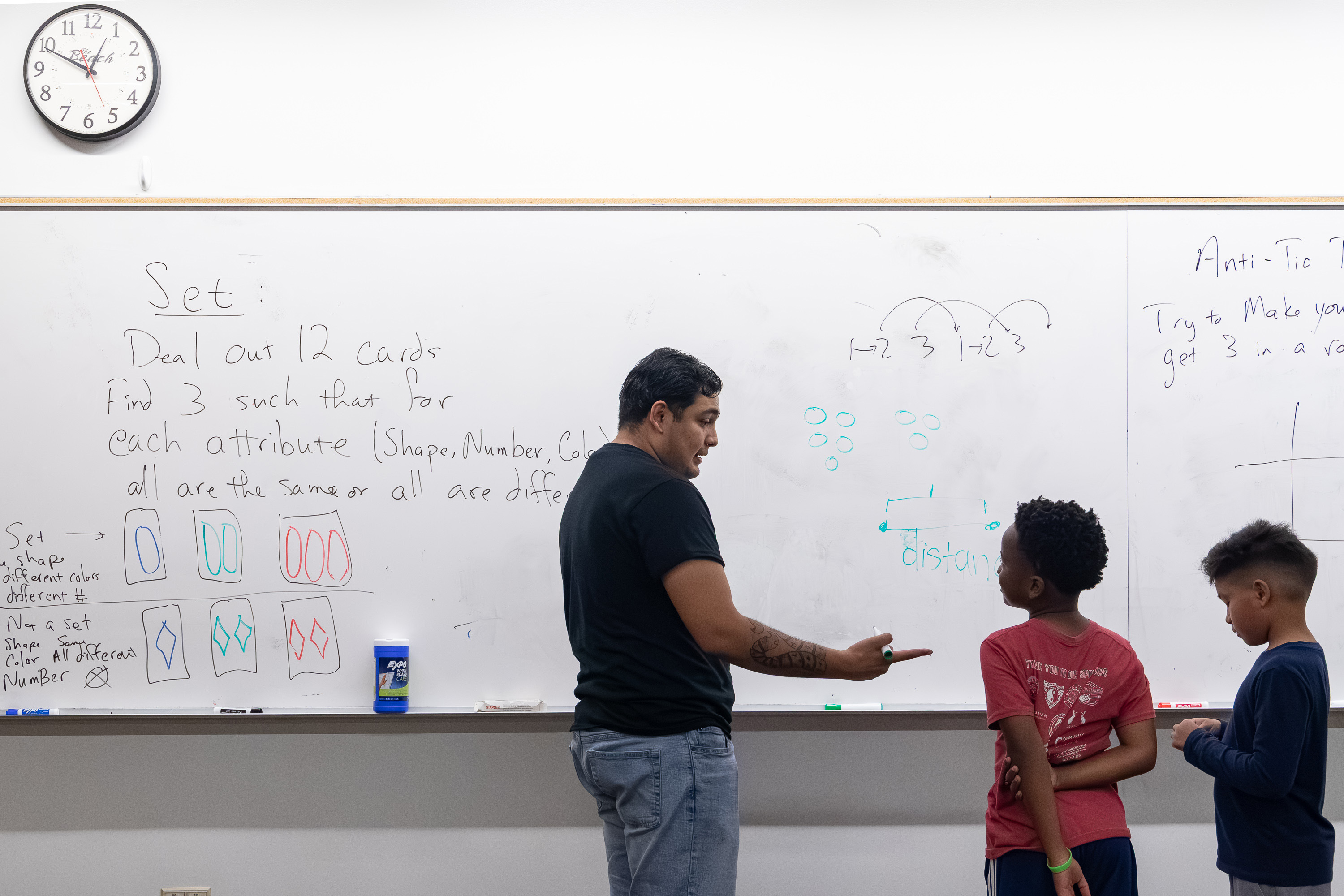 Instructor explains patterns on a whiteboard to two children during a math lesson.