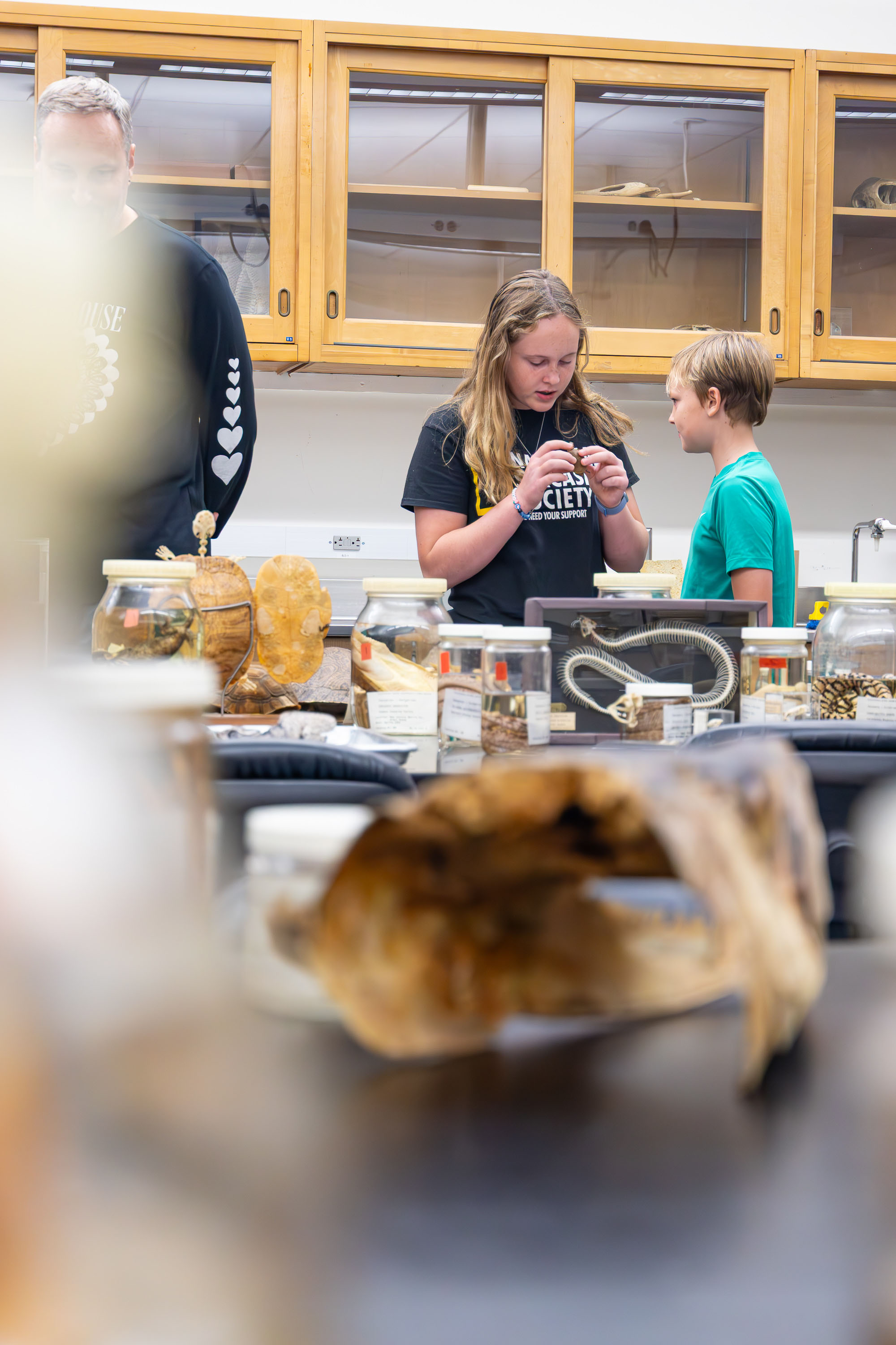 Visitors examine a small specimen in a biology lab surrounded by jars and displays.