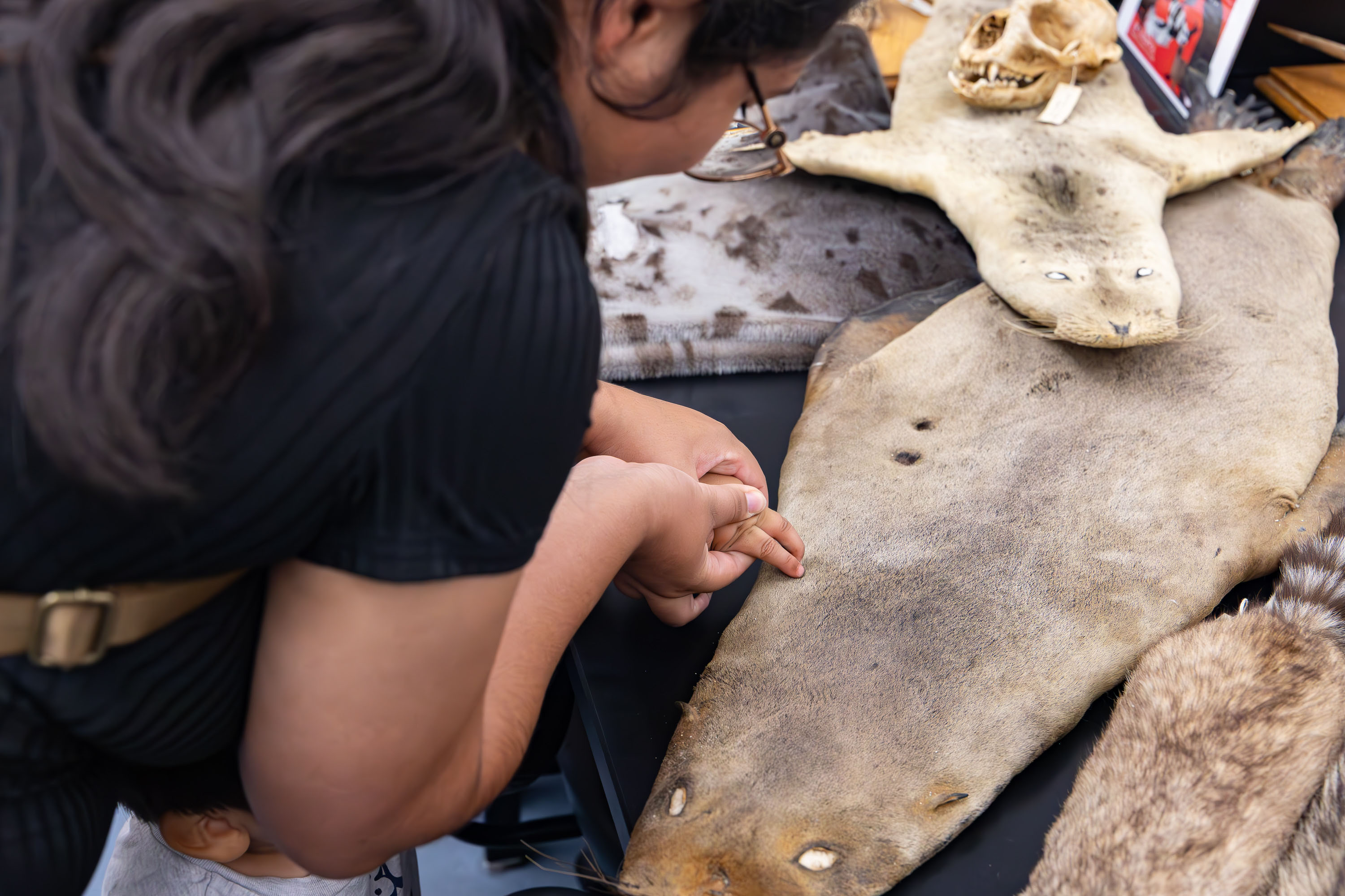 Caregiver guides a child's hand to feel animal pelts at a touch table.