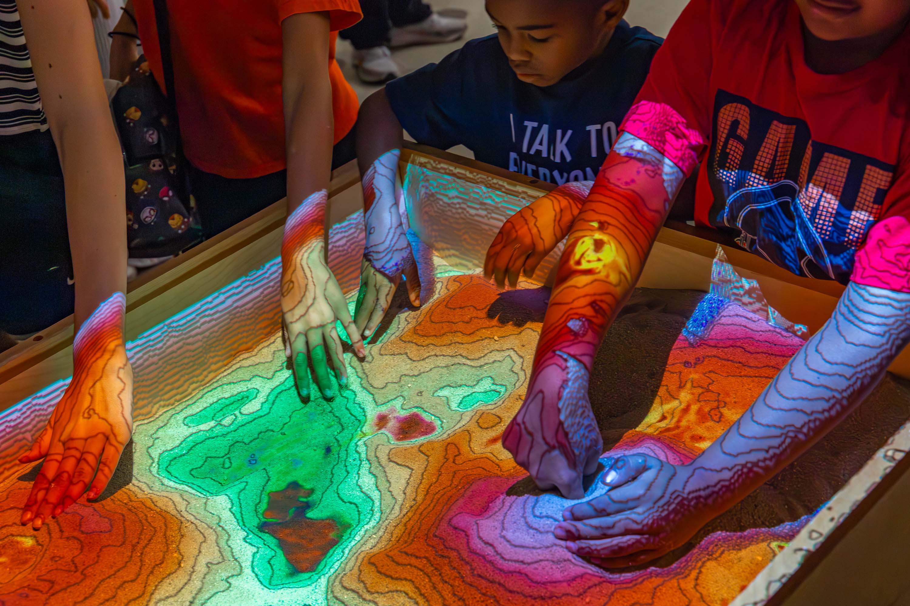 Children shape an augmented reality sandbox displaying contour lines.