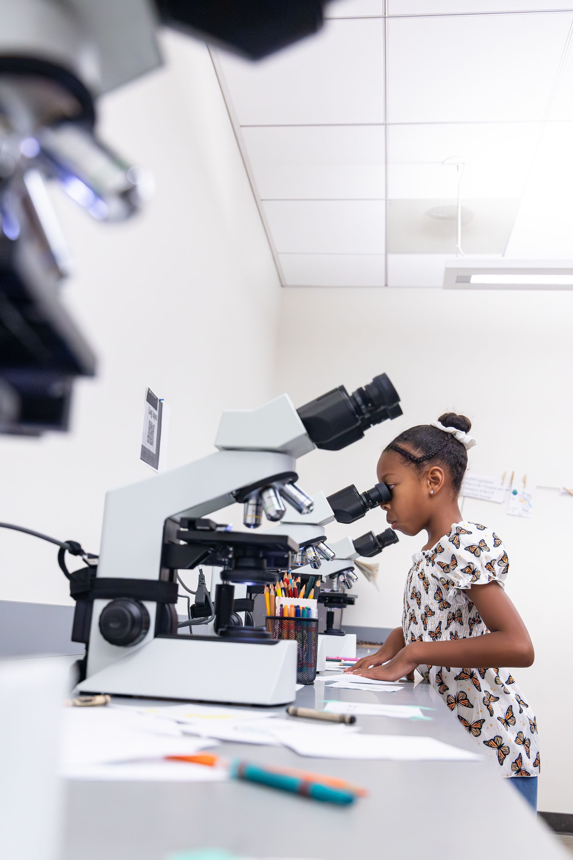 Child looks into a microscope at a lab bench