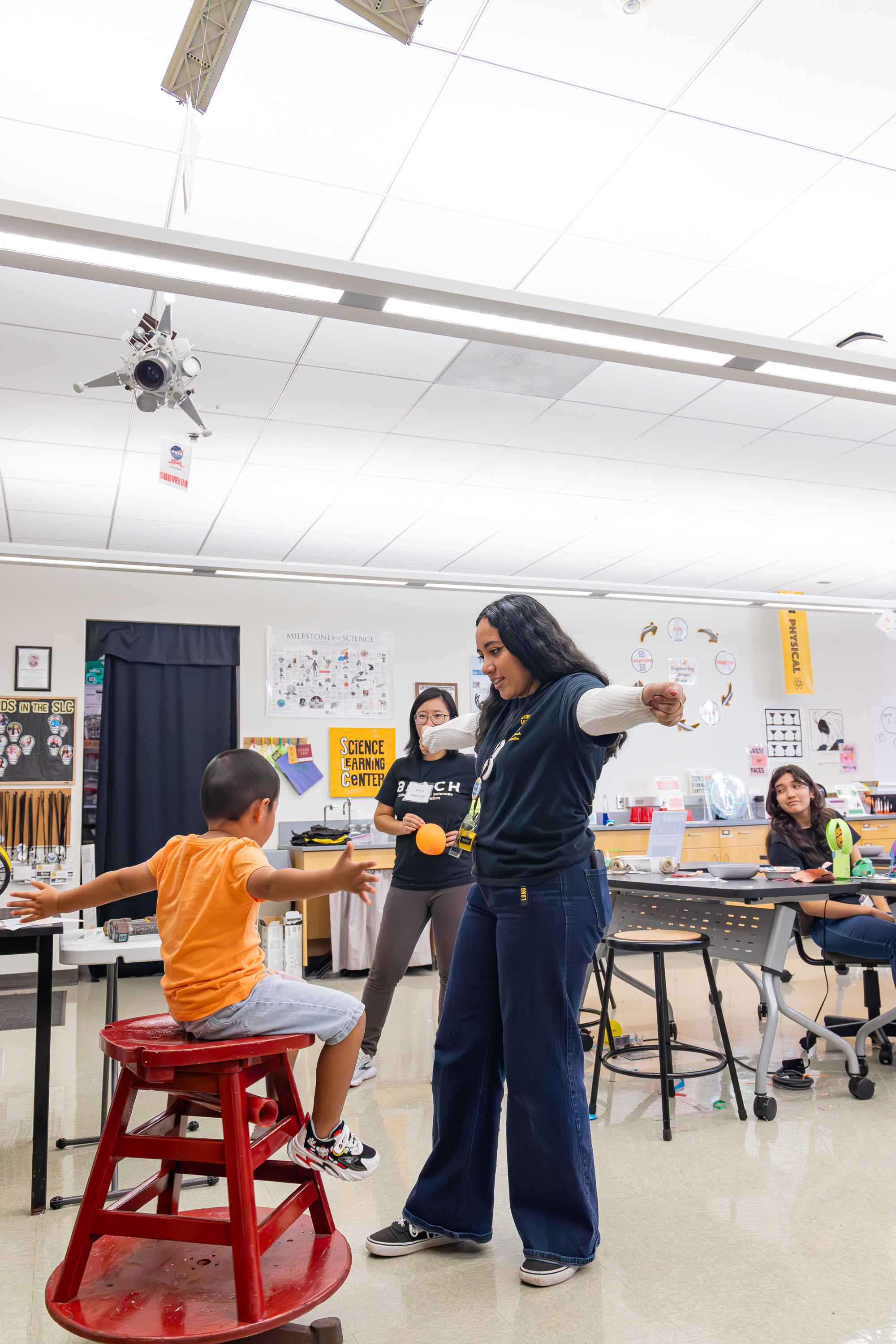 Facilitator leads a physics balance demo with a child on a rotating stool.