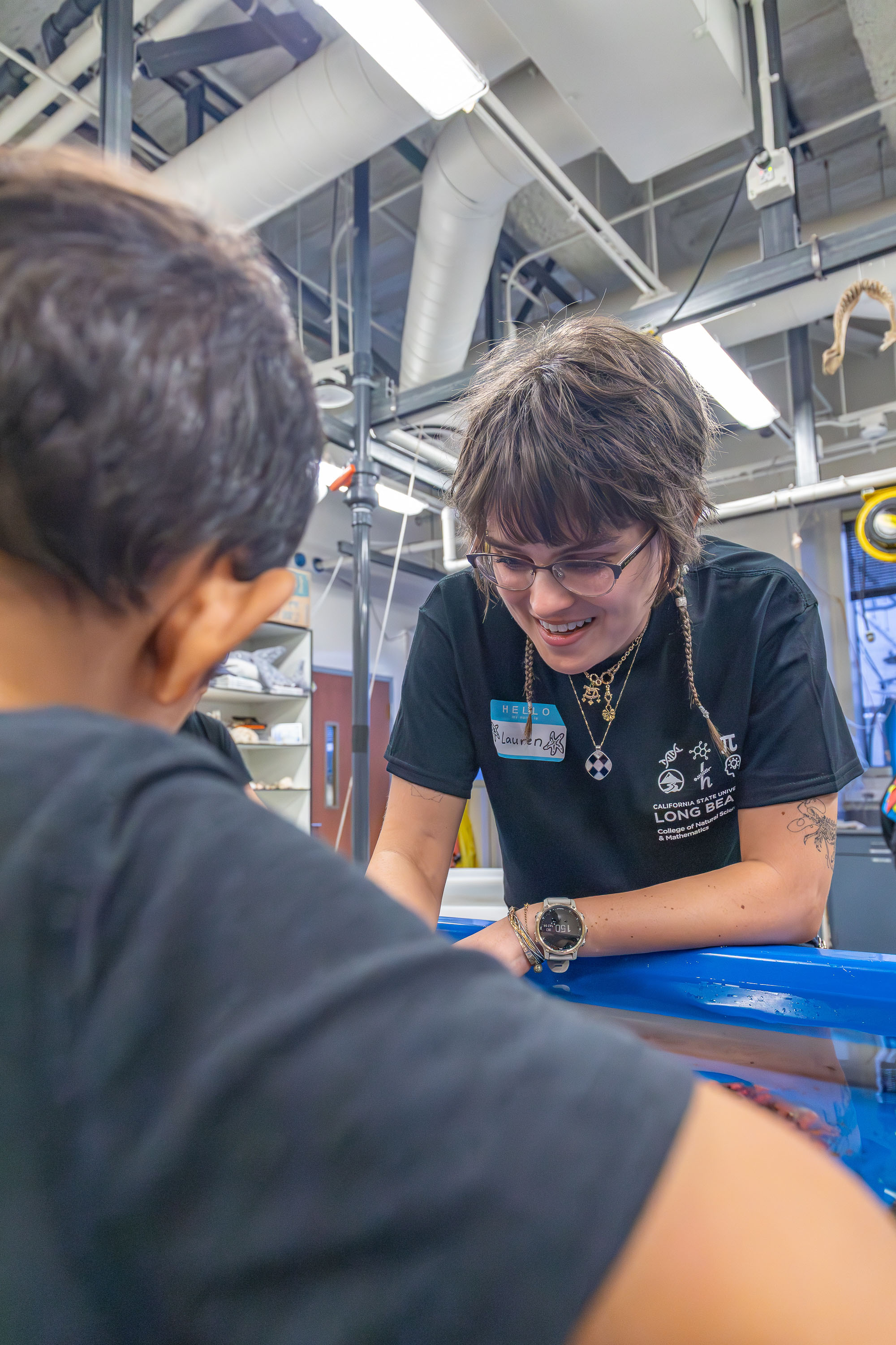 Student volunteer talks with a child at a marine touch tank in a lab.