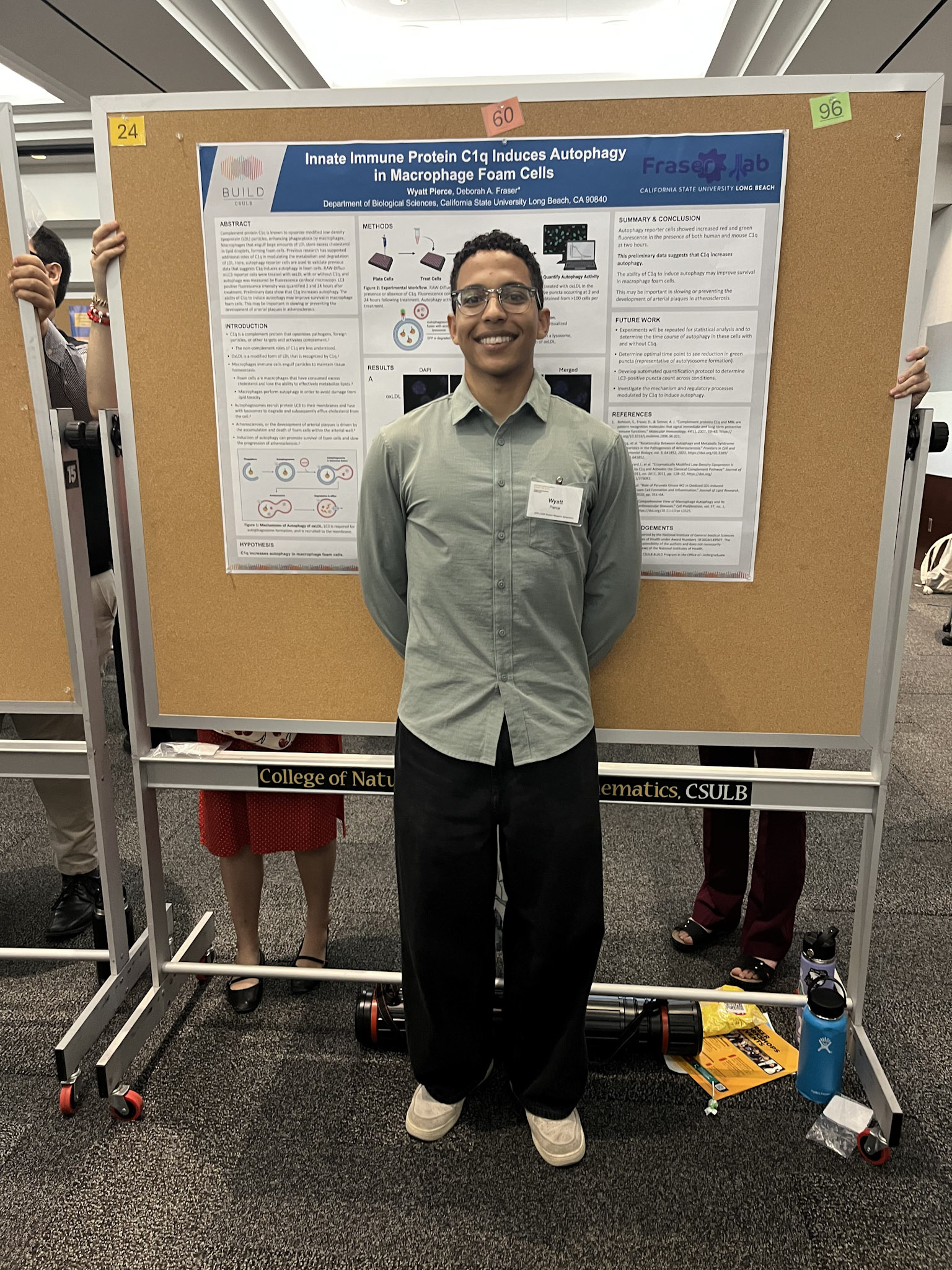 Male presenter with short black hair and green shirt standing in front of research poster