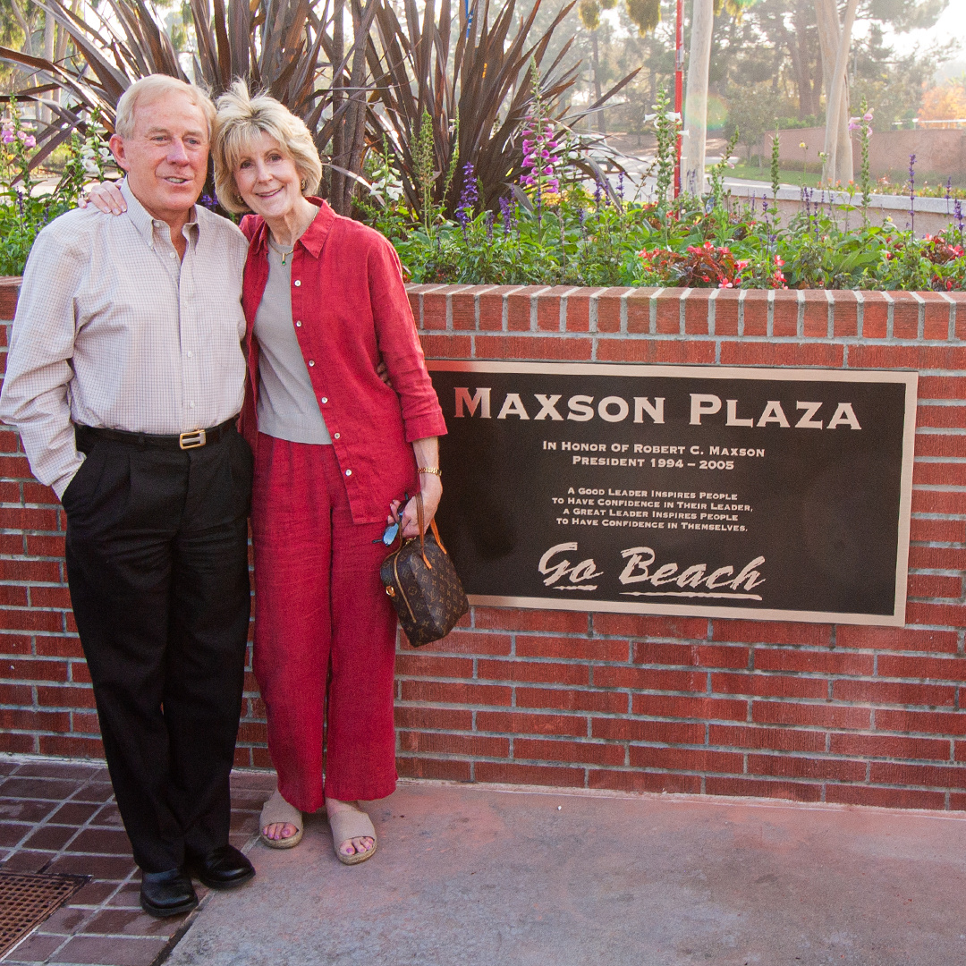 Two people stand beside the Maxson Plaza plaque on campus.