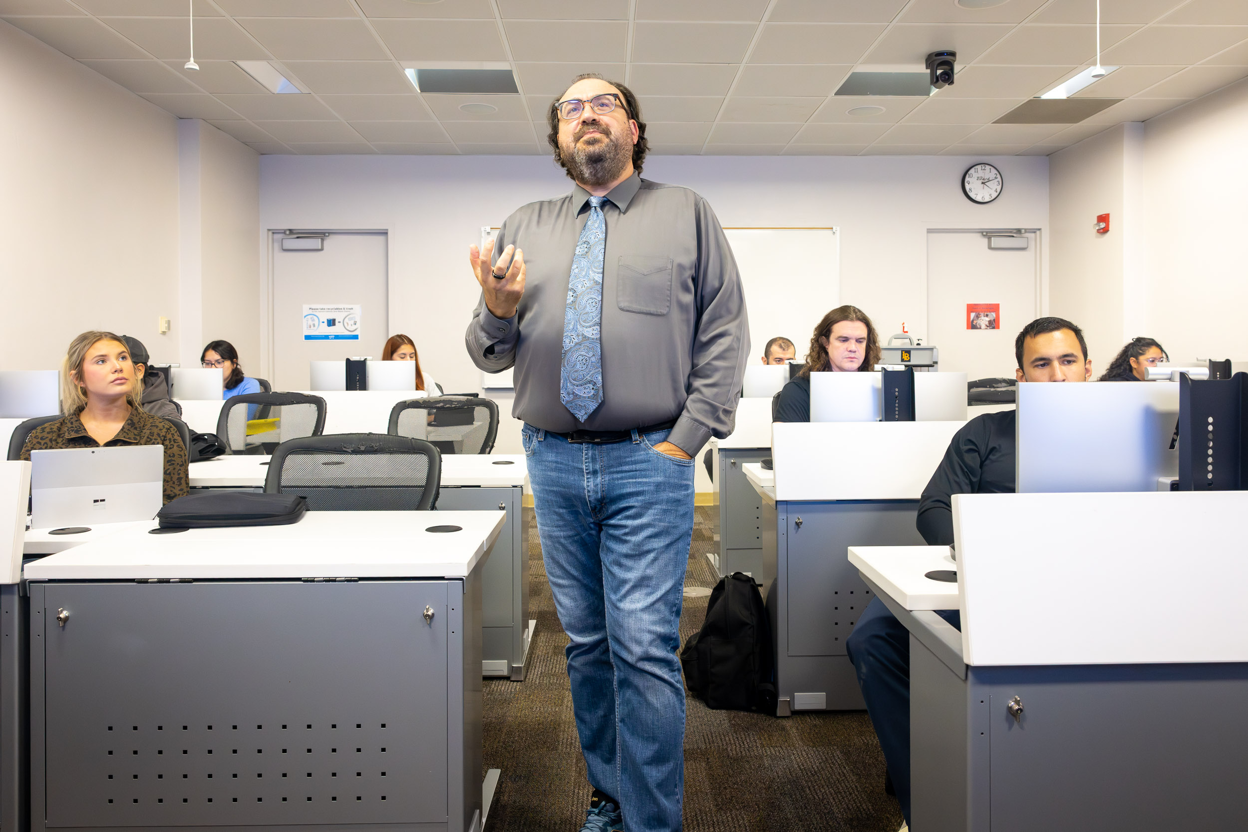  A person wearing jeans and a tie speaks in a classroom 