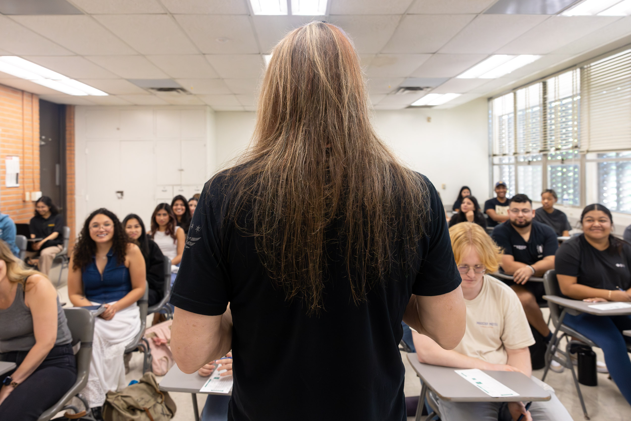 The instructor stands before students who listen and smile during a lecture.