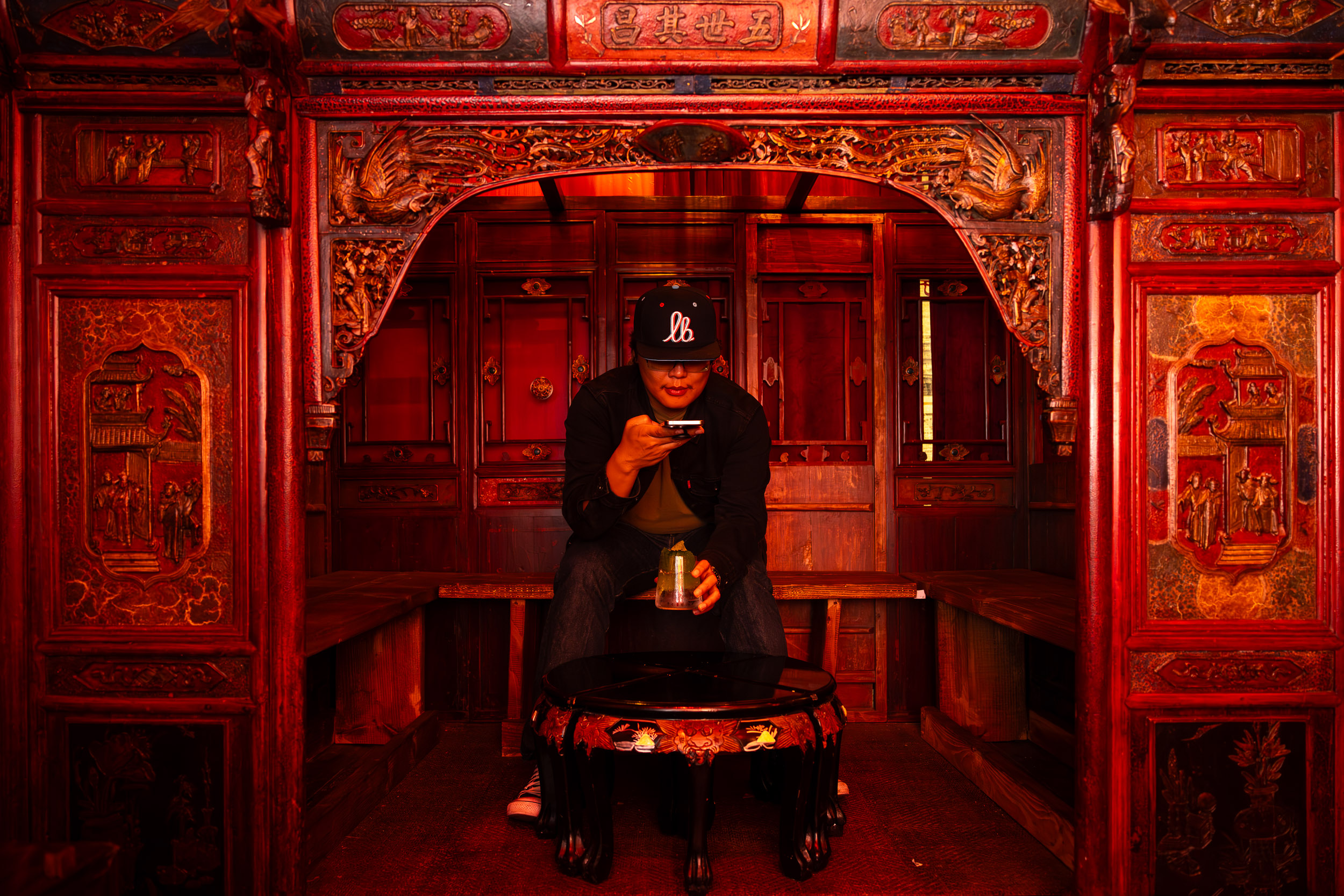 A person in a cap takes a phone photo of a cocktail 