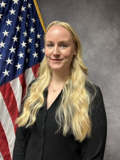 Allyson Joy headshot in front of American flag.