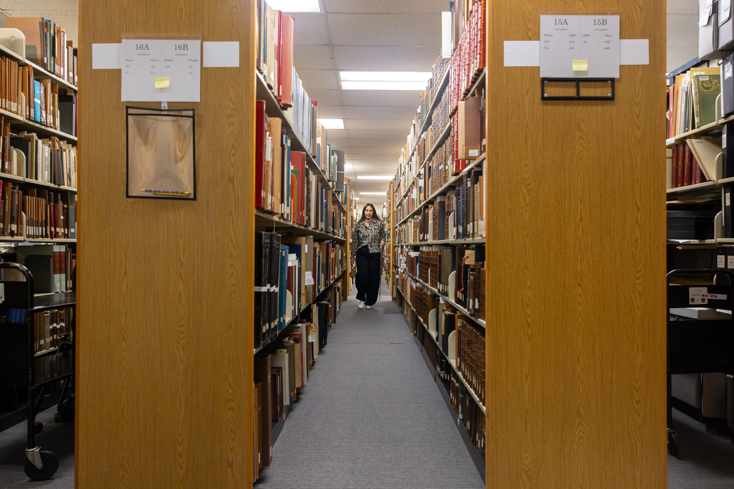 A person walks down an aisle between tall shelves lined with books.