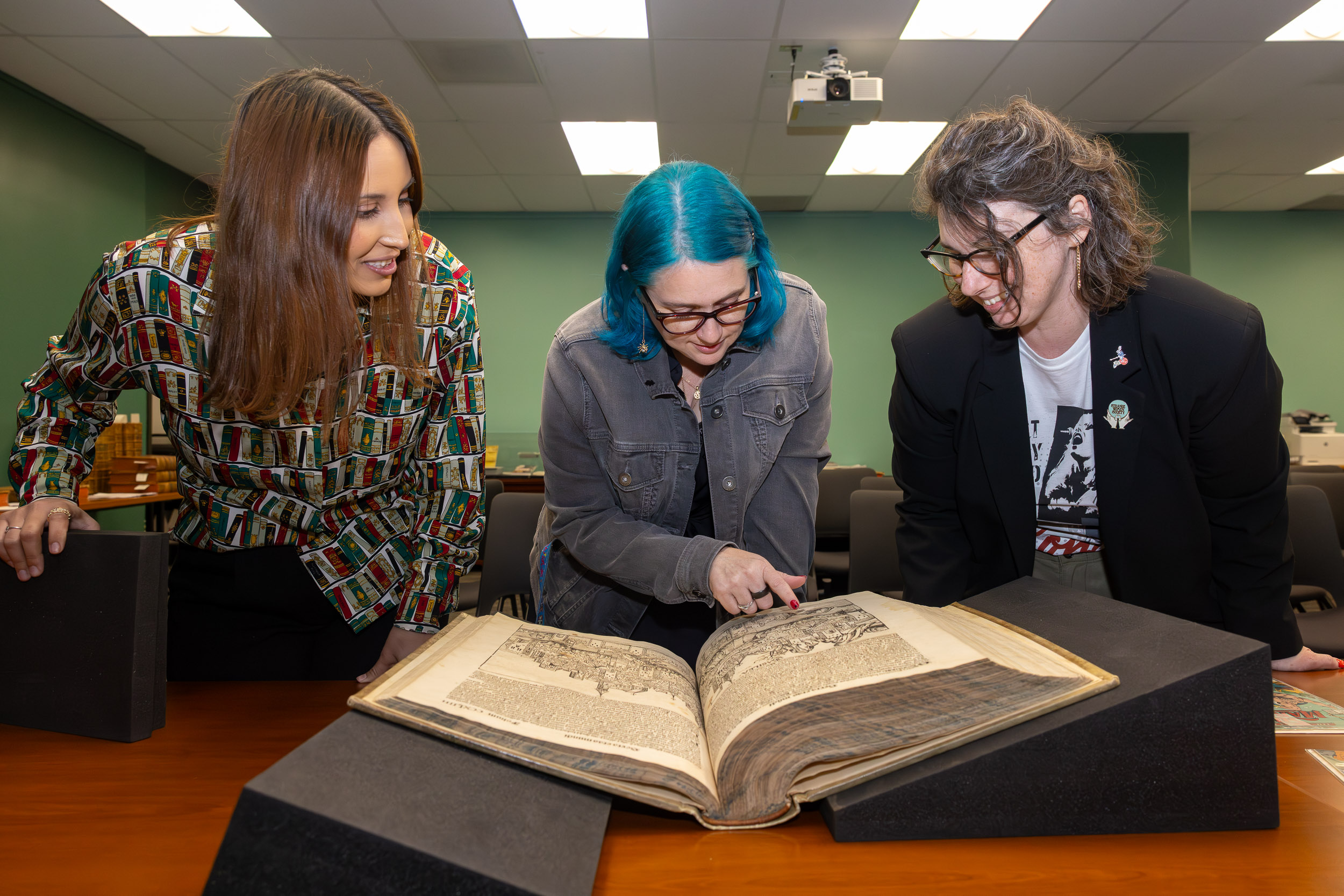 Three people examine an open rare book on a table