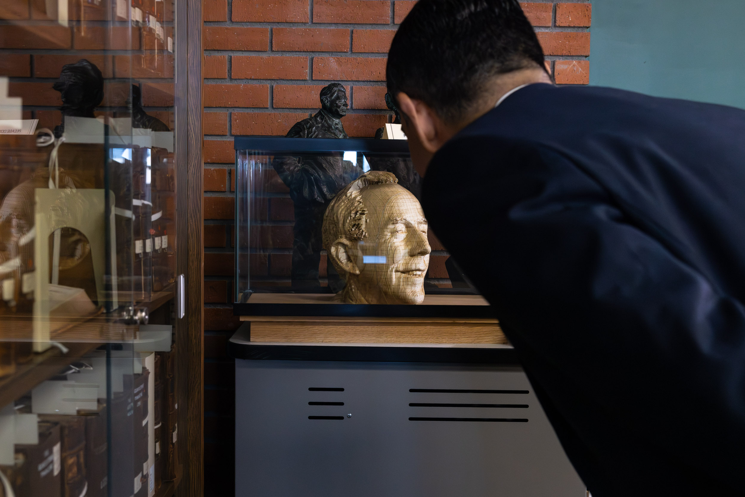 Person leans toward a glass display case holding the Robert Maxson sculpture head.