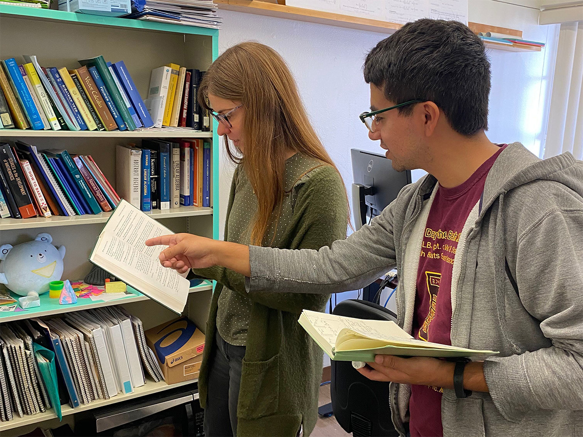 Student researcher pointing to a section in a book that Dr. McCormick is holding