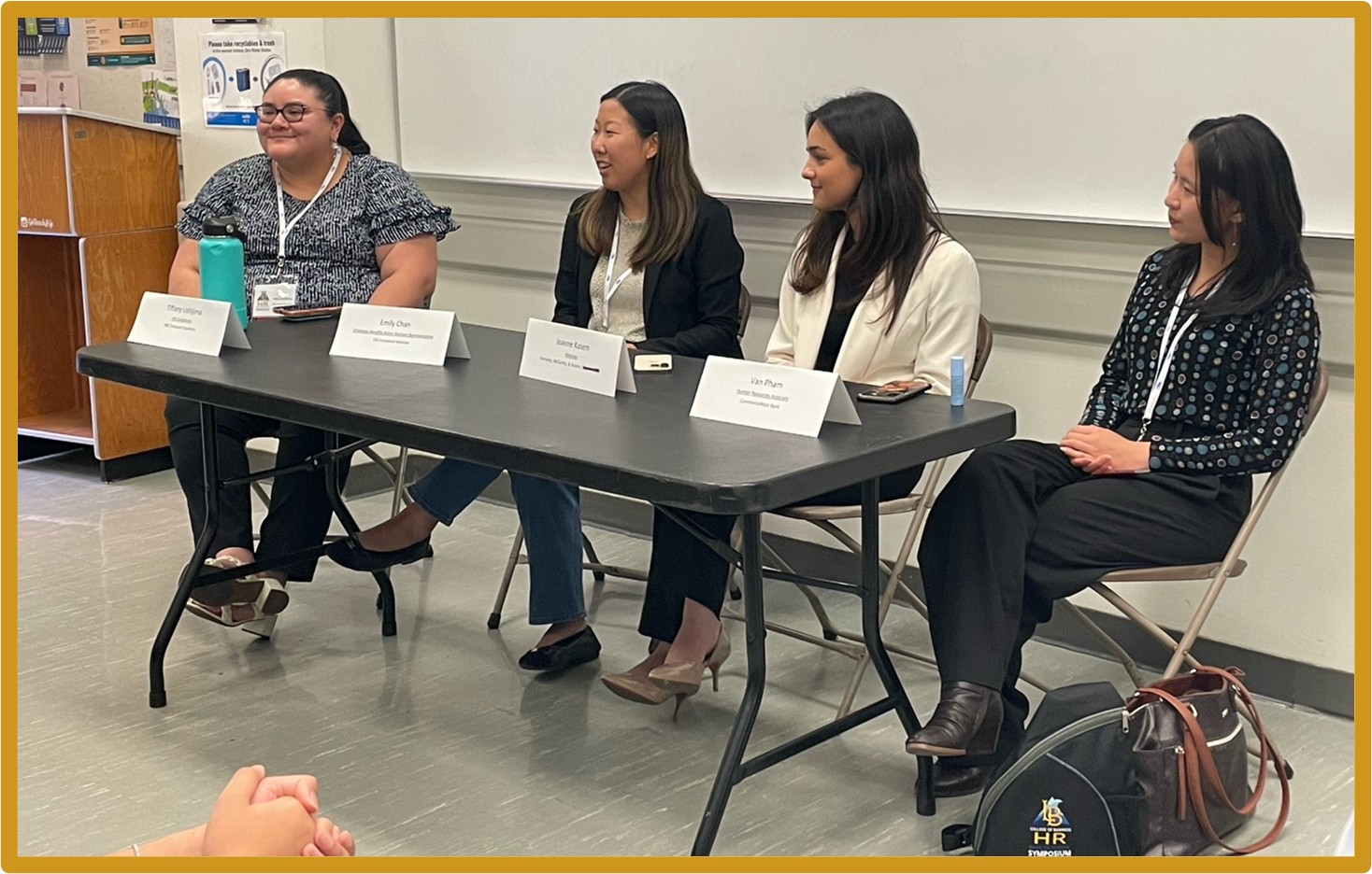 Photo of the four alumni panelists at the HR Symposium at a table listening to the audience