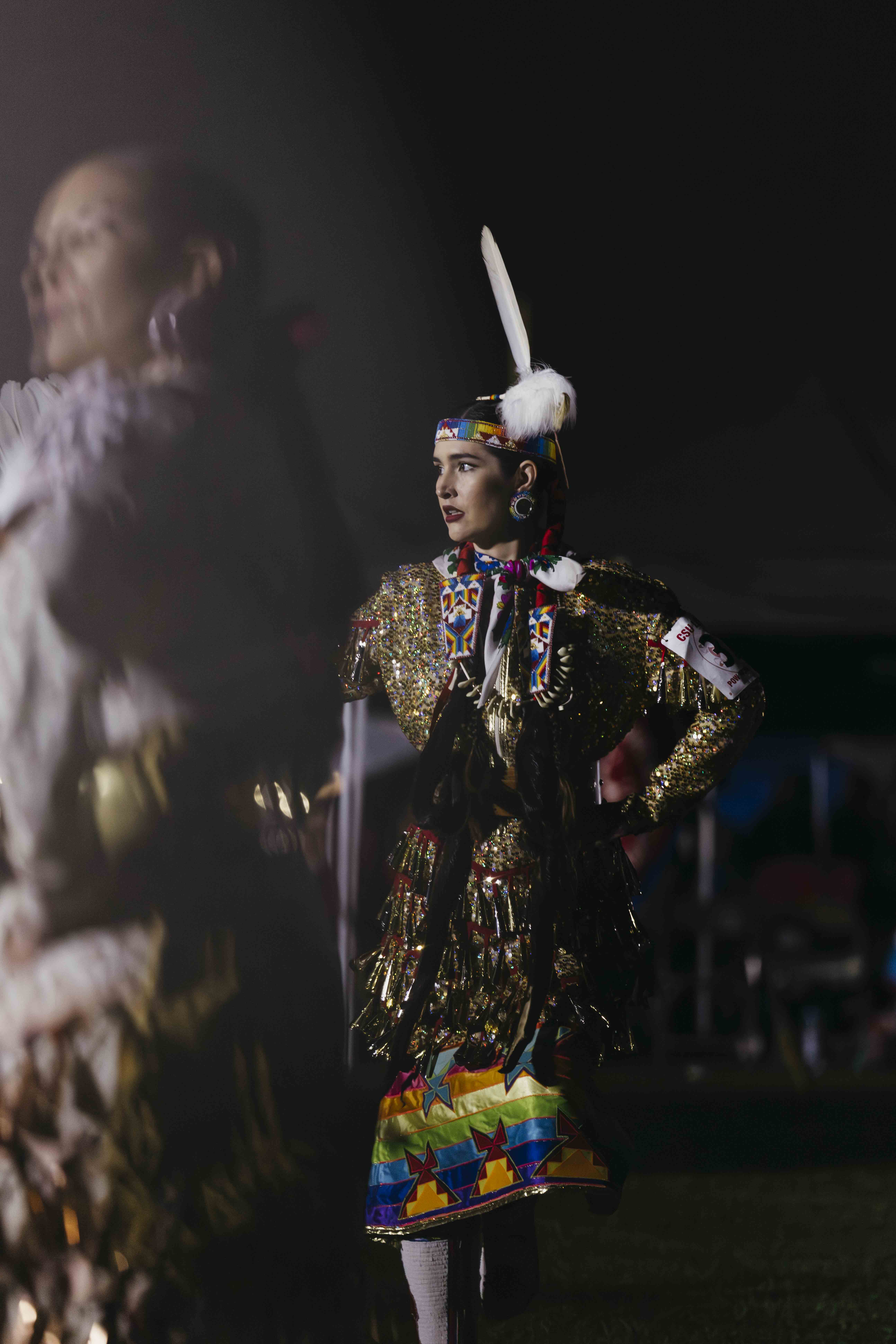 A woman wearing regalia at the 2026 CSULB Pow Wow at night.