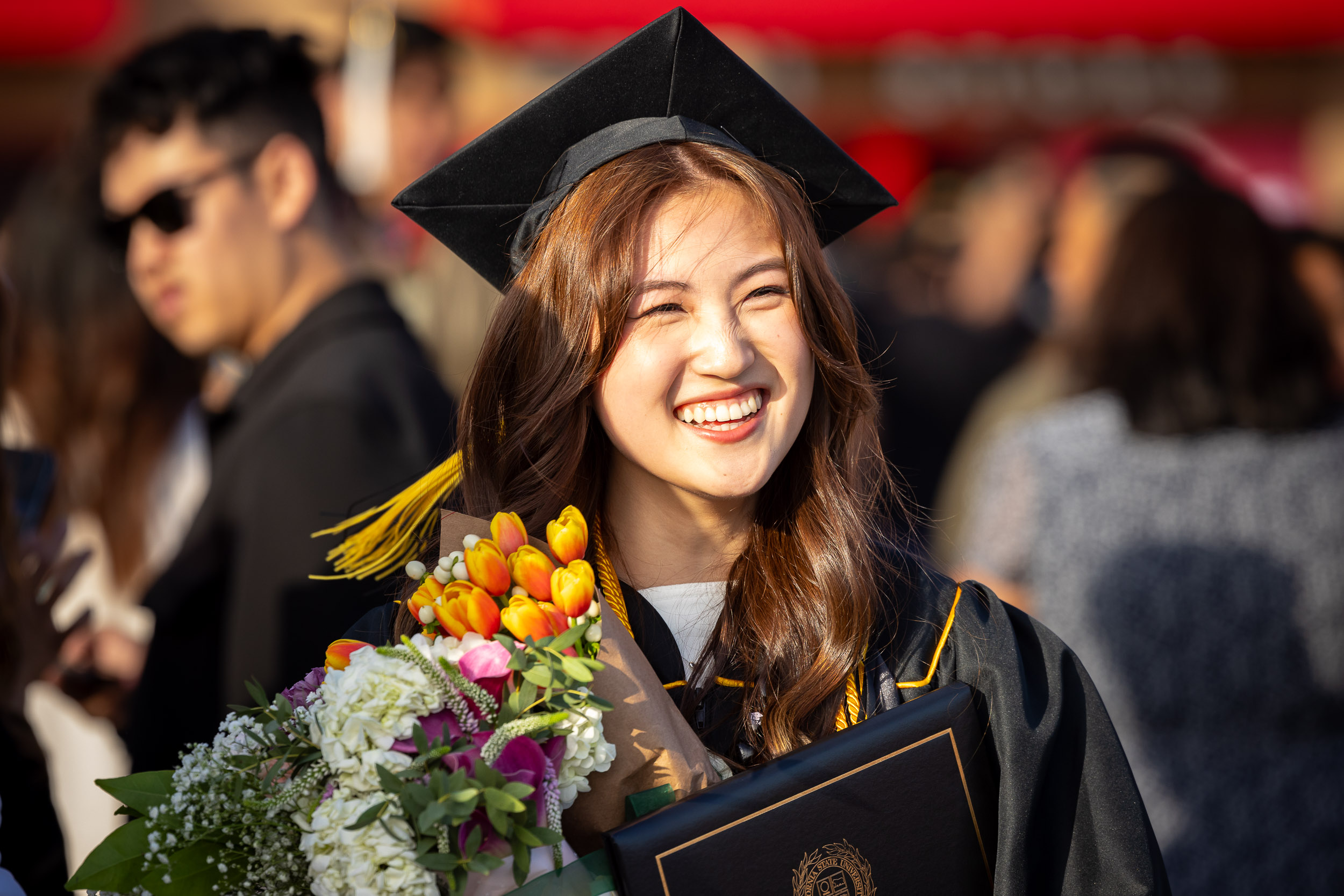 A smiling CSULB graduate with flowers