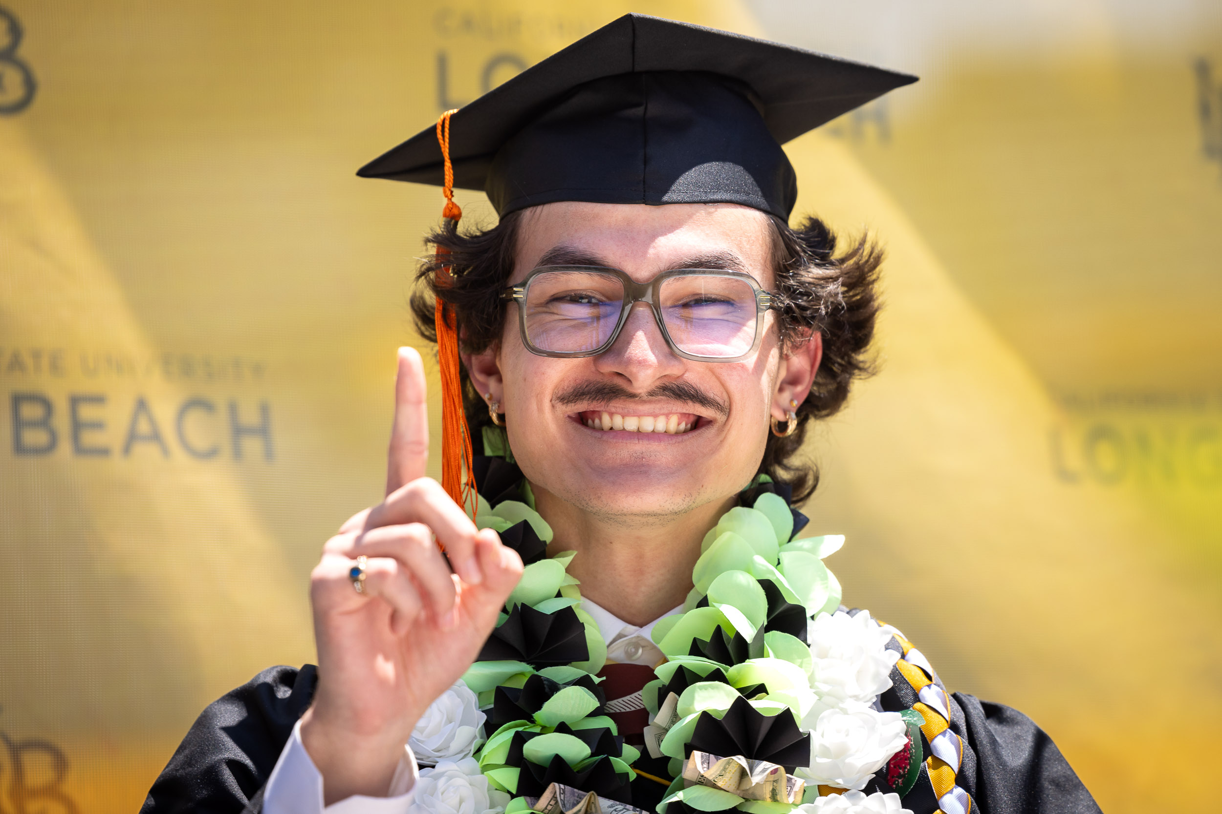 A CSULB grad pointing an inedex finger upward toward his mortarboard