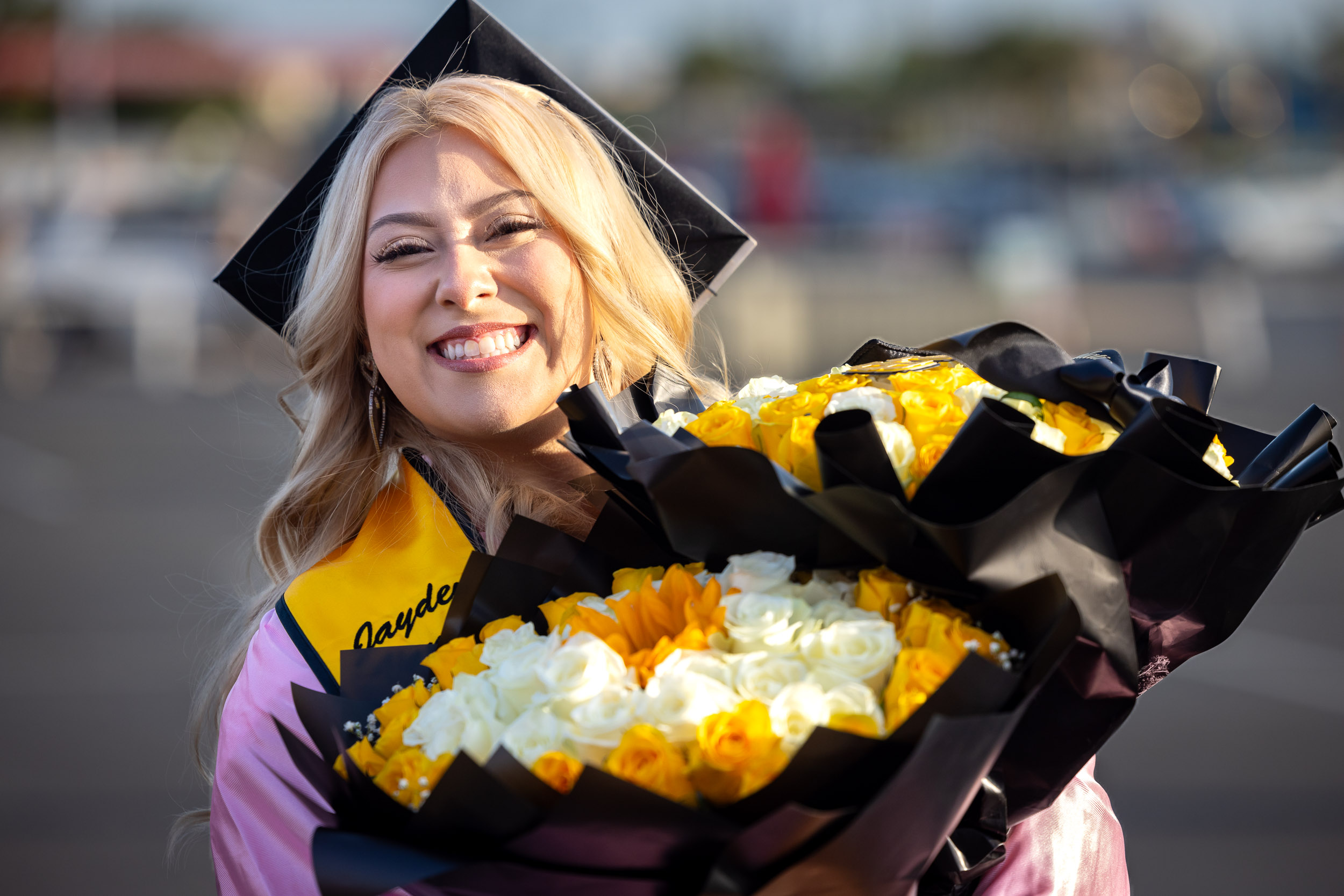 A CSULB graduate holding two bouquets