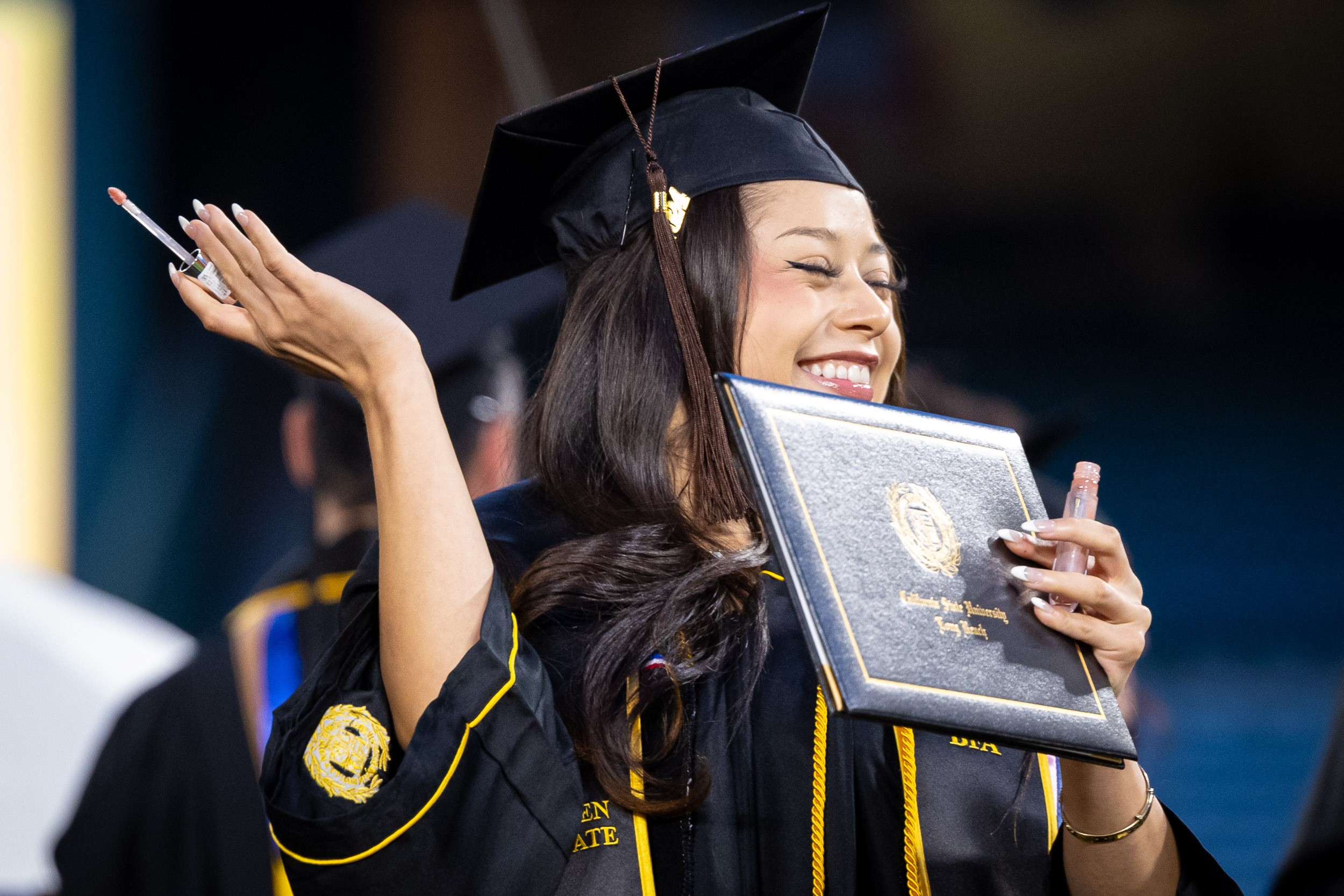 A CSULB graduate holding her diploma and cosmetics